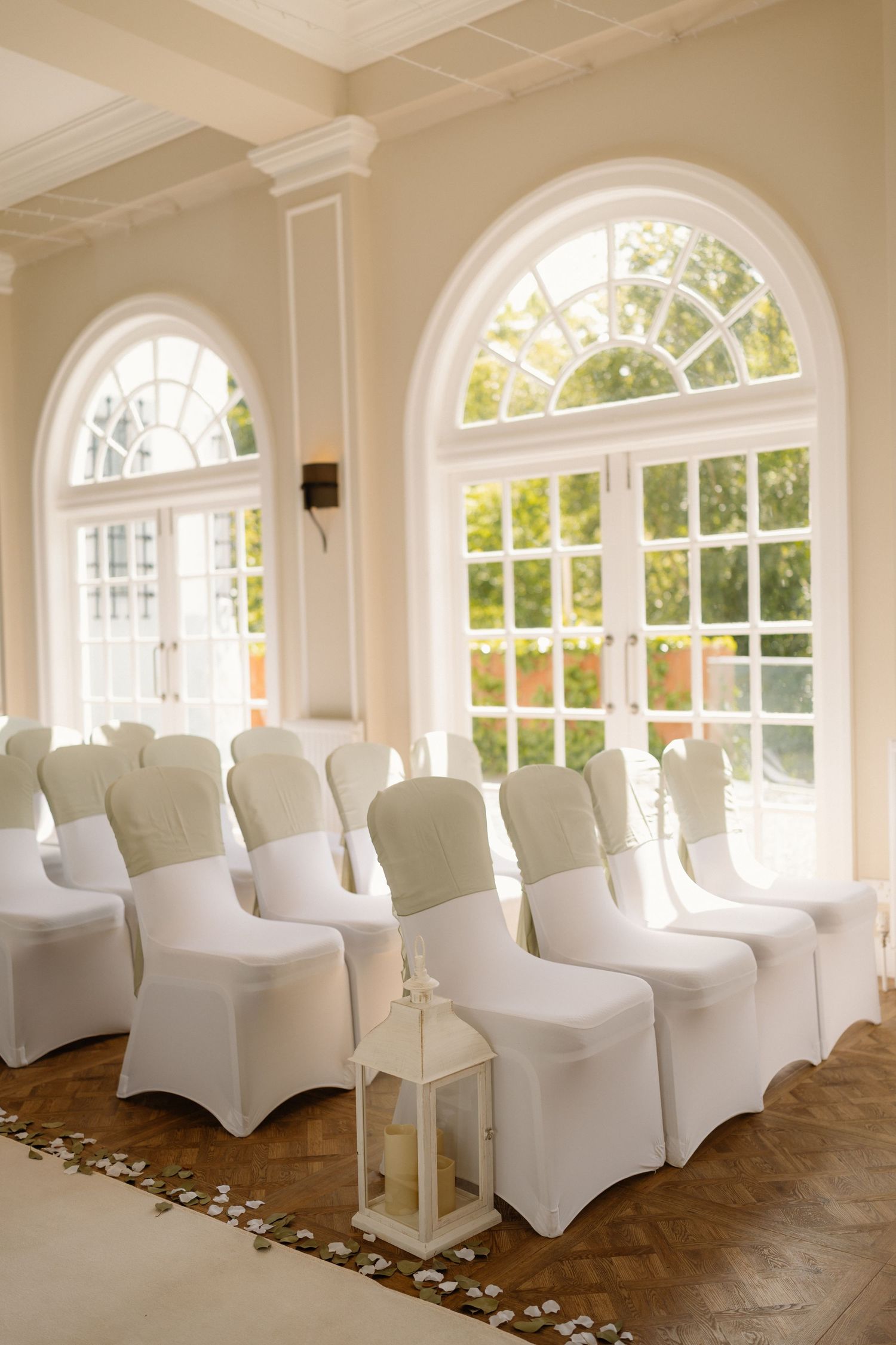 Elegant wedding ceremony room with white chair covers and large arched windows with natural light.