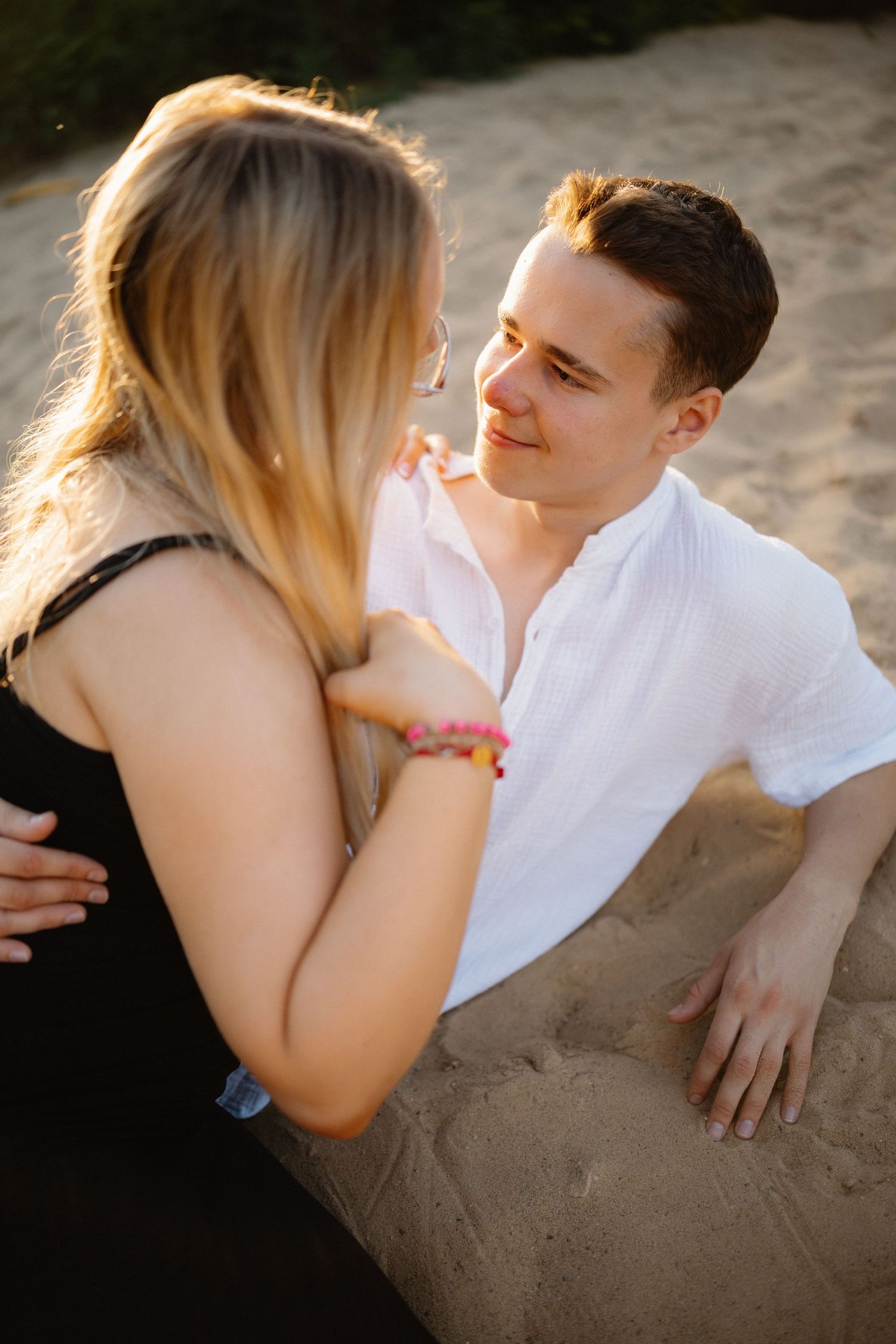 Couple shares tender moment while sitting on sandy beach at sunset.