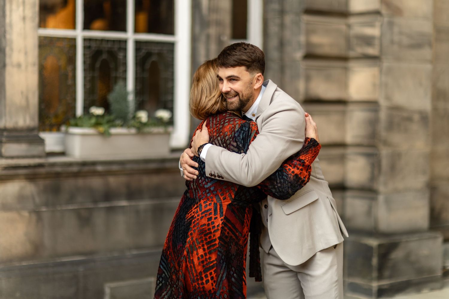 An emotional embrace captured outside a historic stone building.