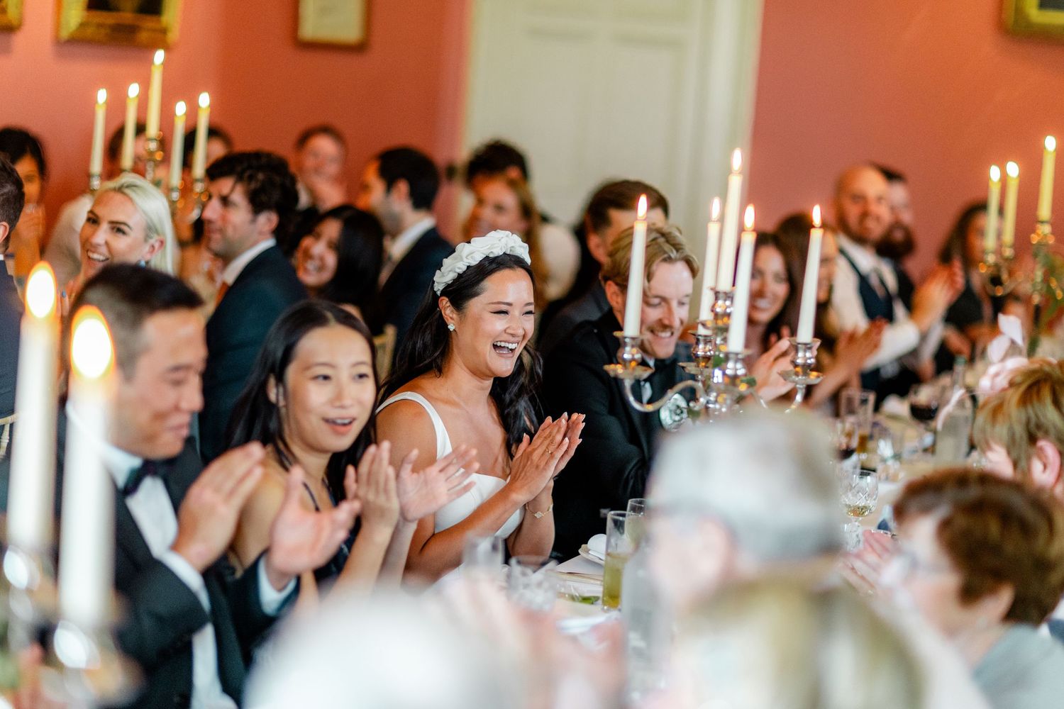 Wedding guests laughing and celebrating at an elegant candlelit reception dinner.