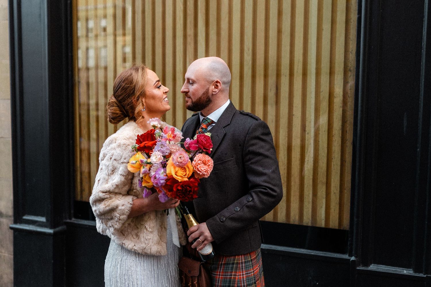 A couple shares a romantic moment in front of a wooden paneled wall during their wedding celebration.