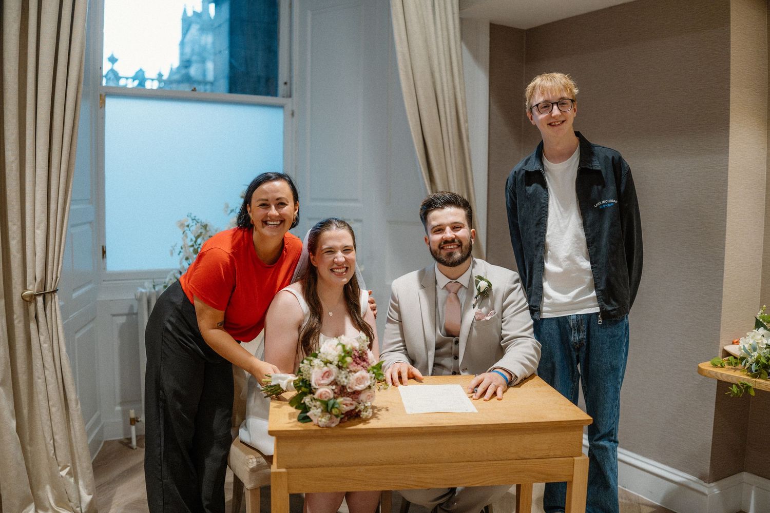 People gathered around a wooden dining table with yellow flowers in a bright interior space.