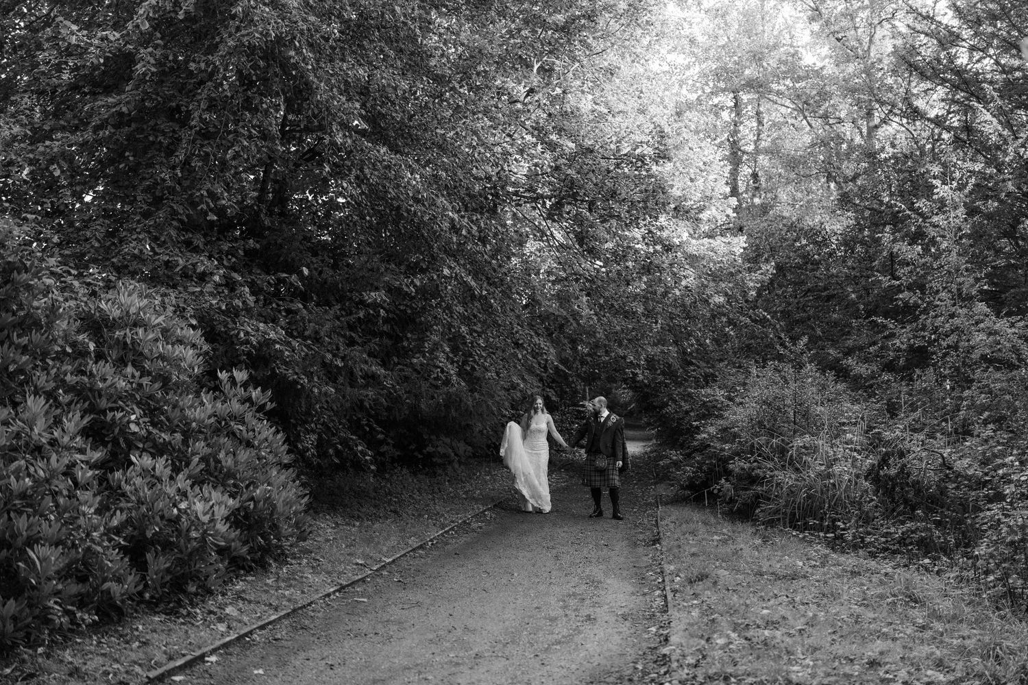 A wooded pathway through dense trees and foliage creates a natural tunnel effect in black and white.