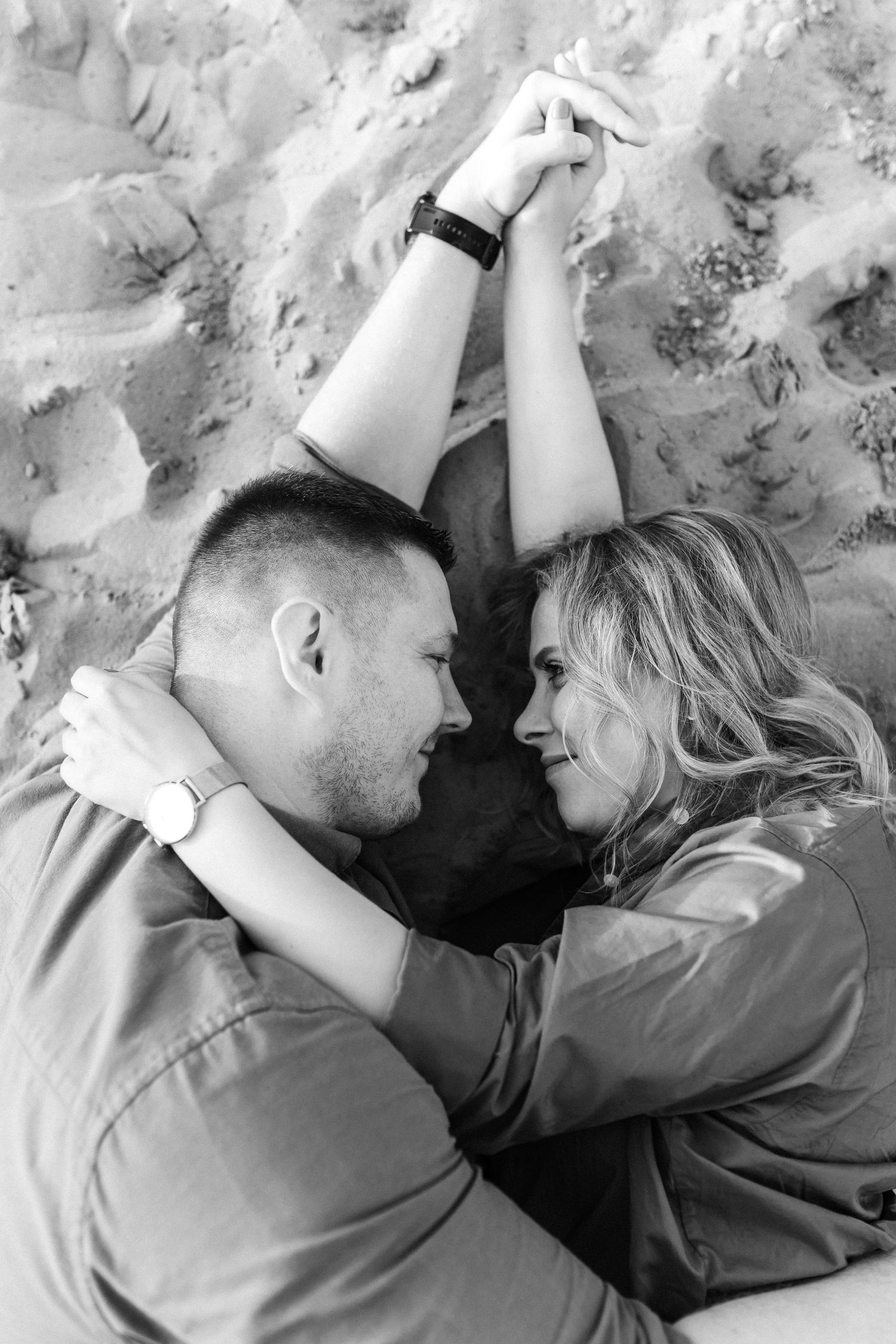 Intimate black and white portraits of couple lying together on textured surface.
