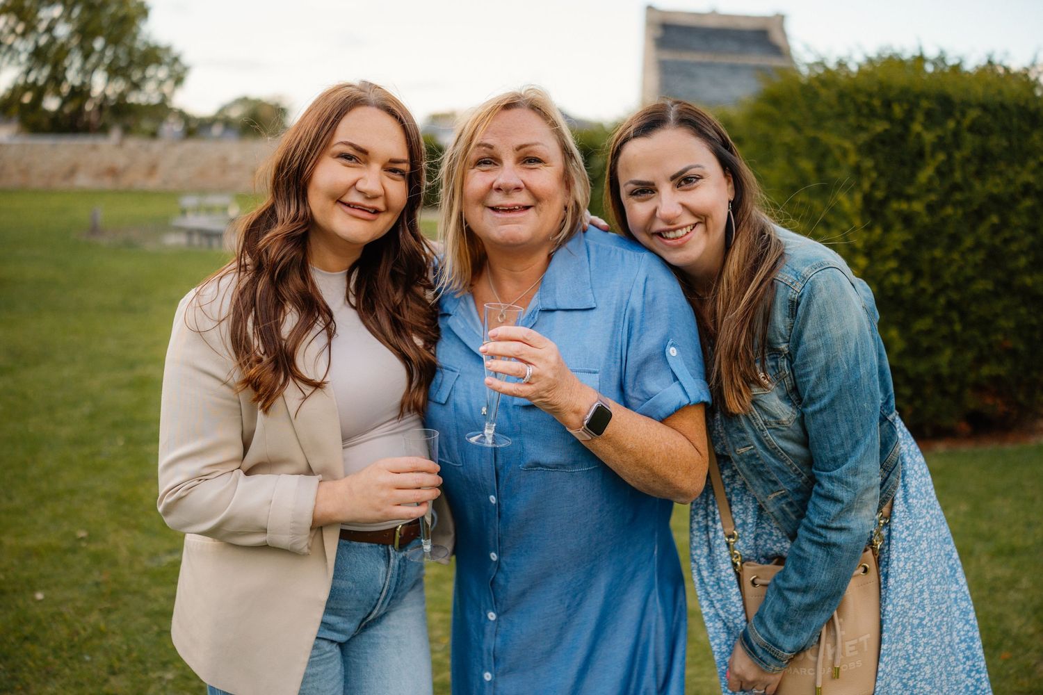 Three women sharing a joyful moment together outdoors on a sunny day.
