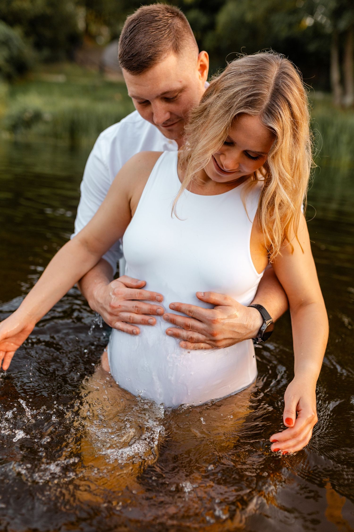 Maternity photoshoot in water showing pregnant woman's belly with splashing effects.