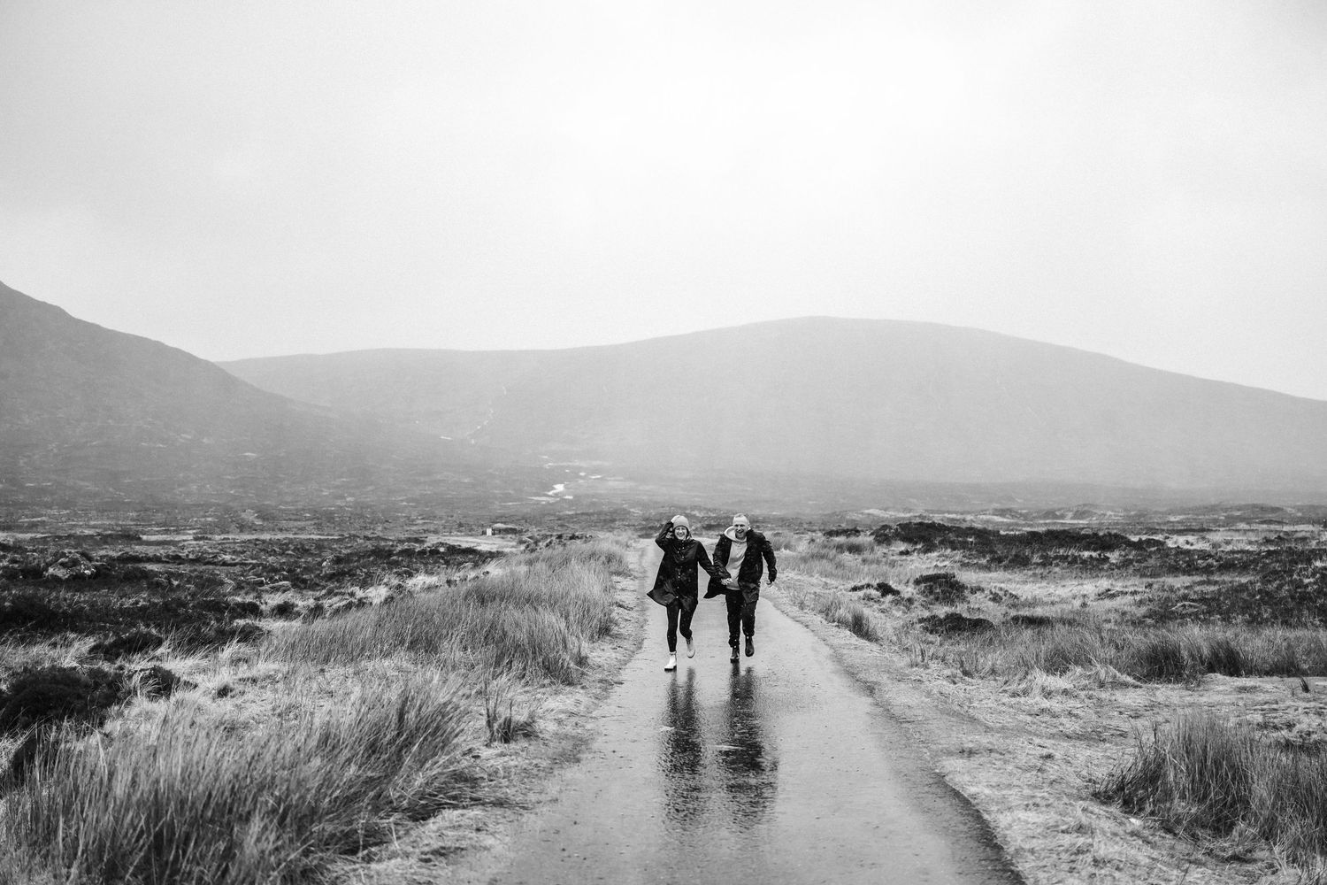 Two silhouettes walking together on a misty path through rolling hills.