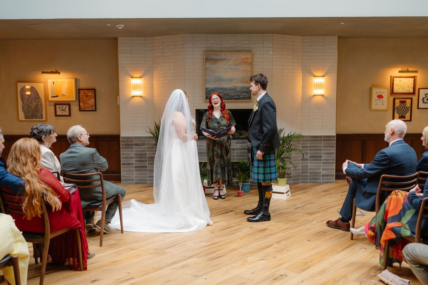 Bride and groom exchange vows during an intimate wedding ceremony in a warmly lit venue with seated guests.