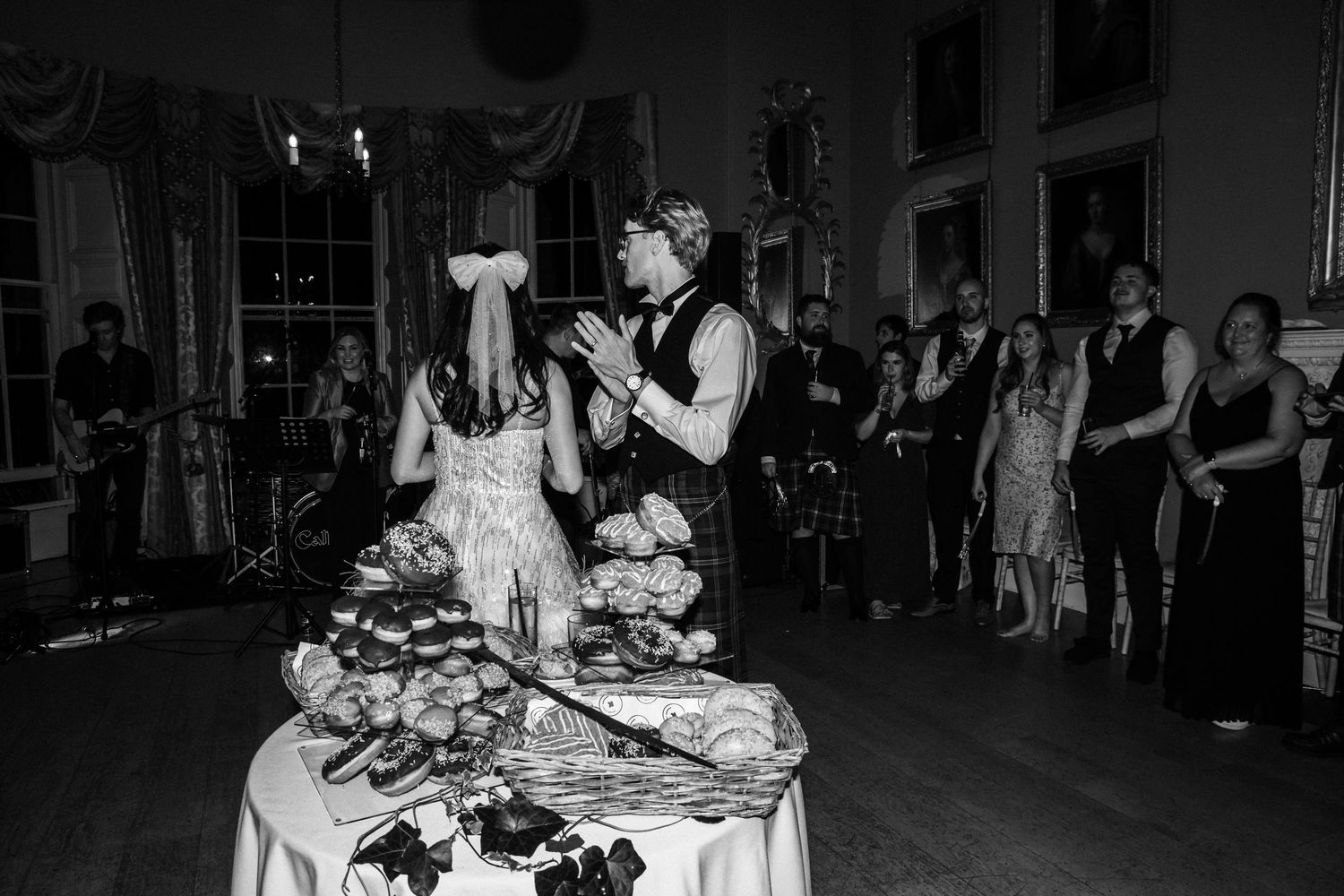 Wedding reception celebration with couple near dessert table surrounded by guests.