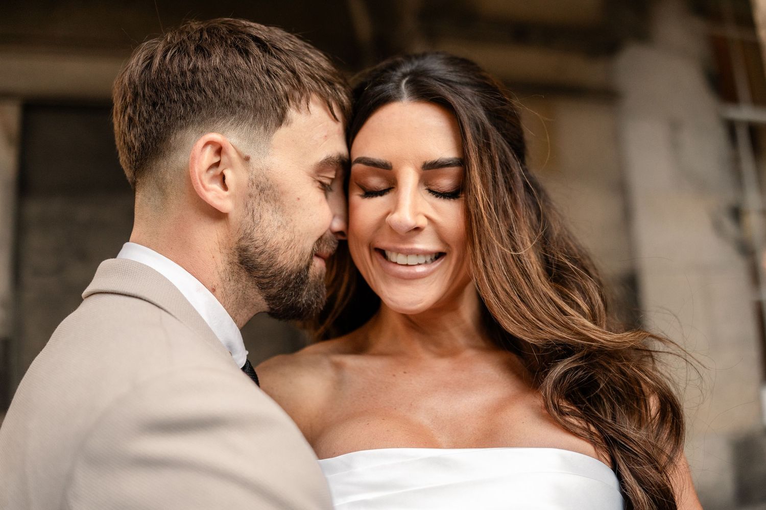 Intimate moment between newlyweds against stone building backdrop.