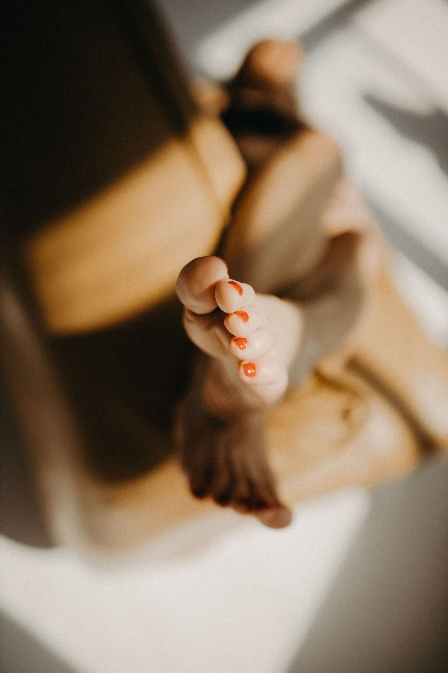 Close-up shot of feet with orange painted toenails against a blurred background in warm lighting.