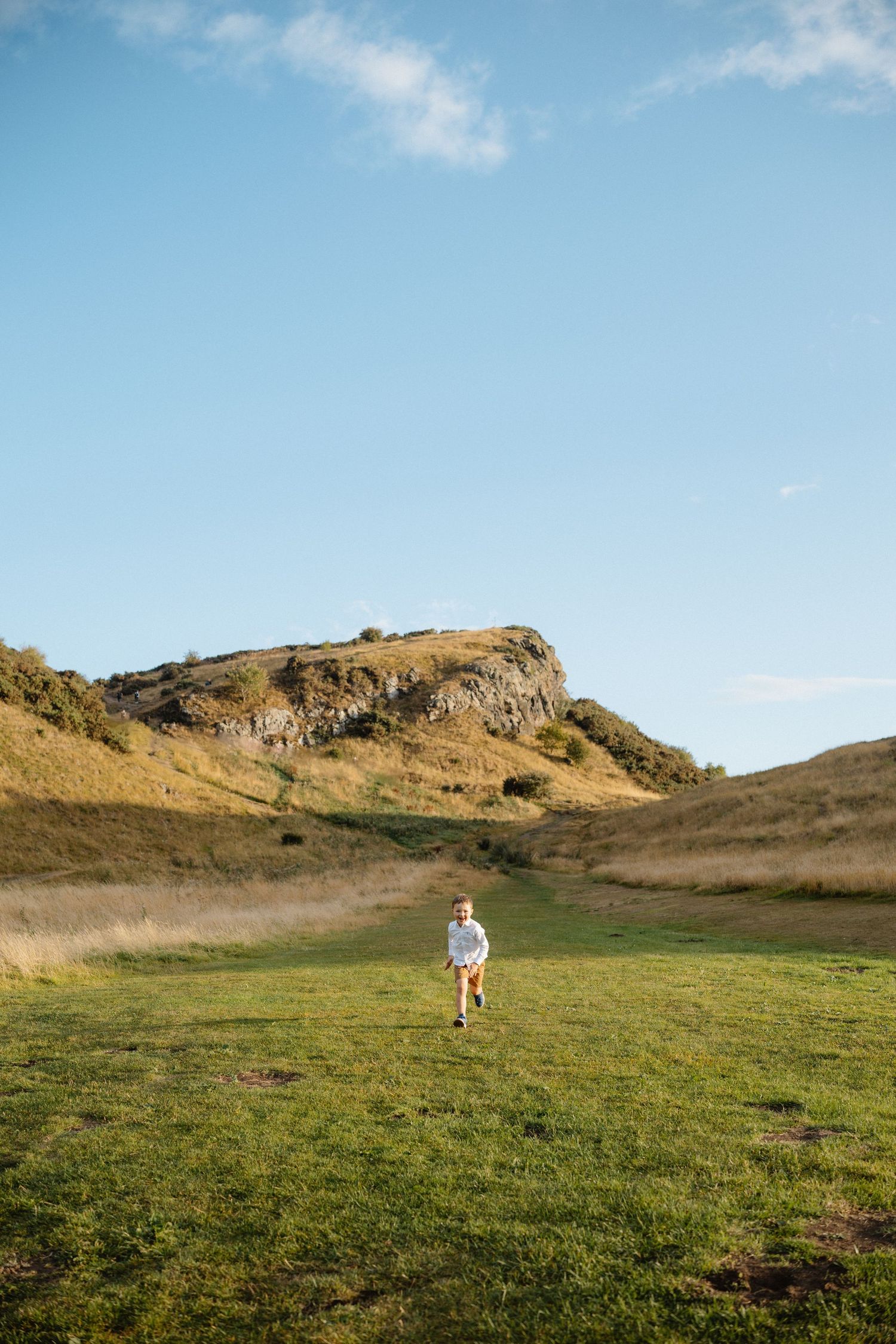 Rolling hills and rocky outcrops against bright blue sky in pastoral landscape.