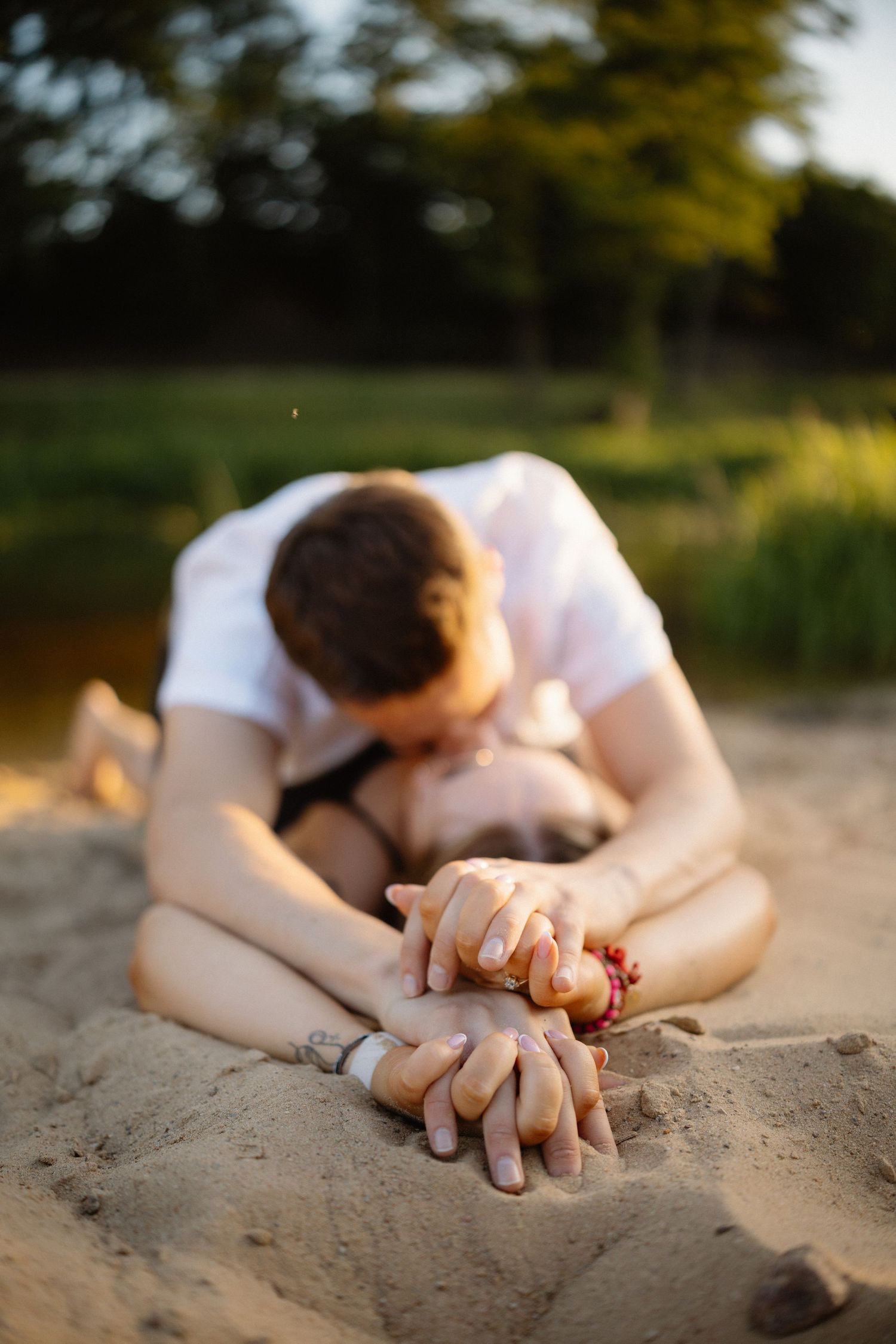 Close-up of hands intertwined on sandy beach during sunset photoshoot.