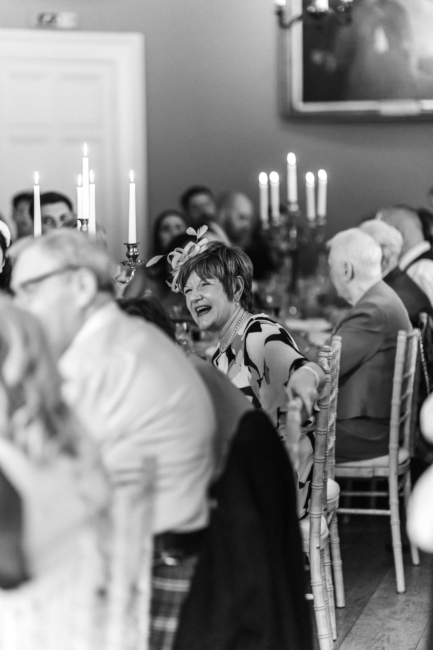 Black and white photo of candlelit wedding reception with guests laughing.