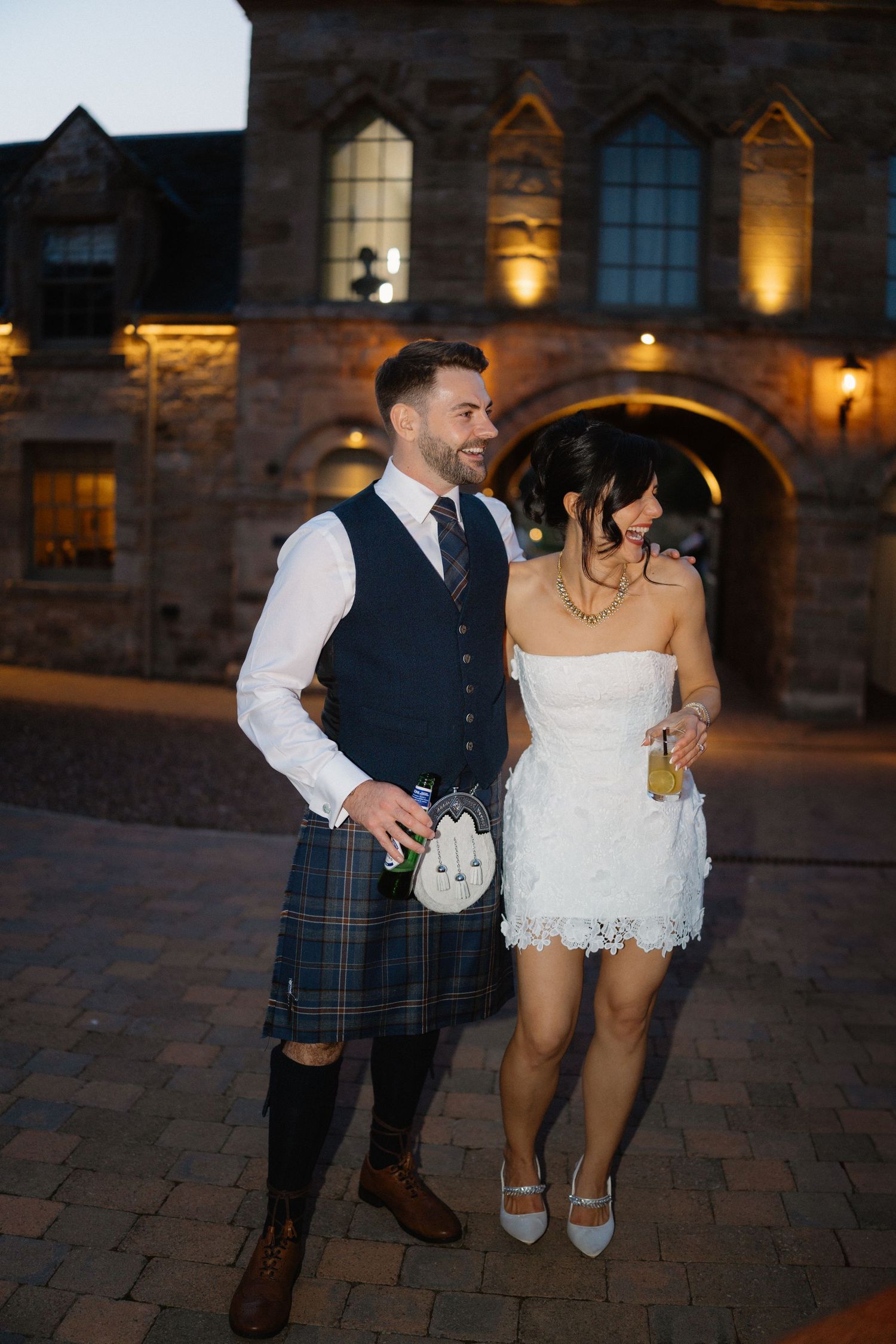 Couple walking together on cobblestone path outside historic building at night.