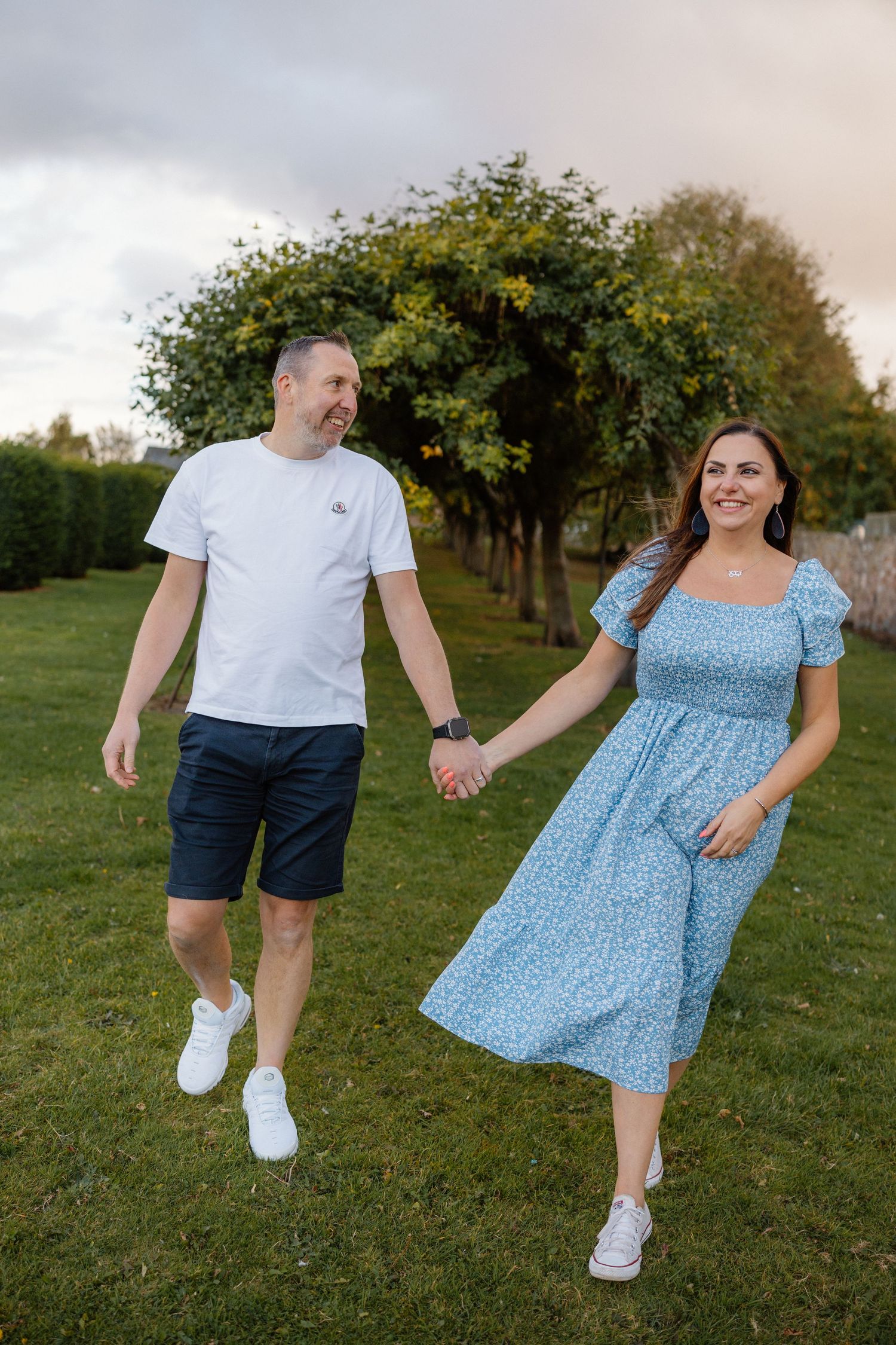 Playful couple dancing and twirling in a grassy park setting.