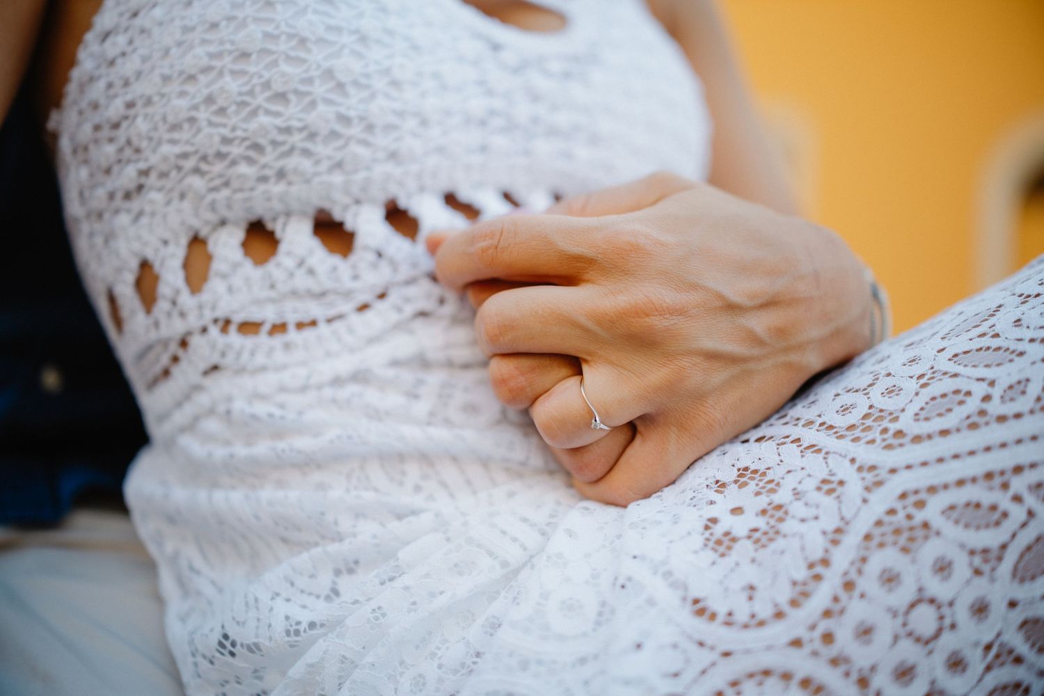 Close up of intricate white lace pattern on dress with hands visible.