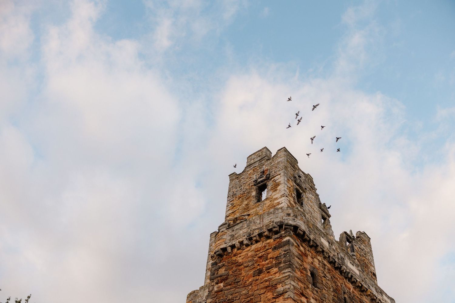 Ancient stone tower ruins with birds flying overhead against a partly cloudy sky.