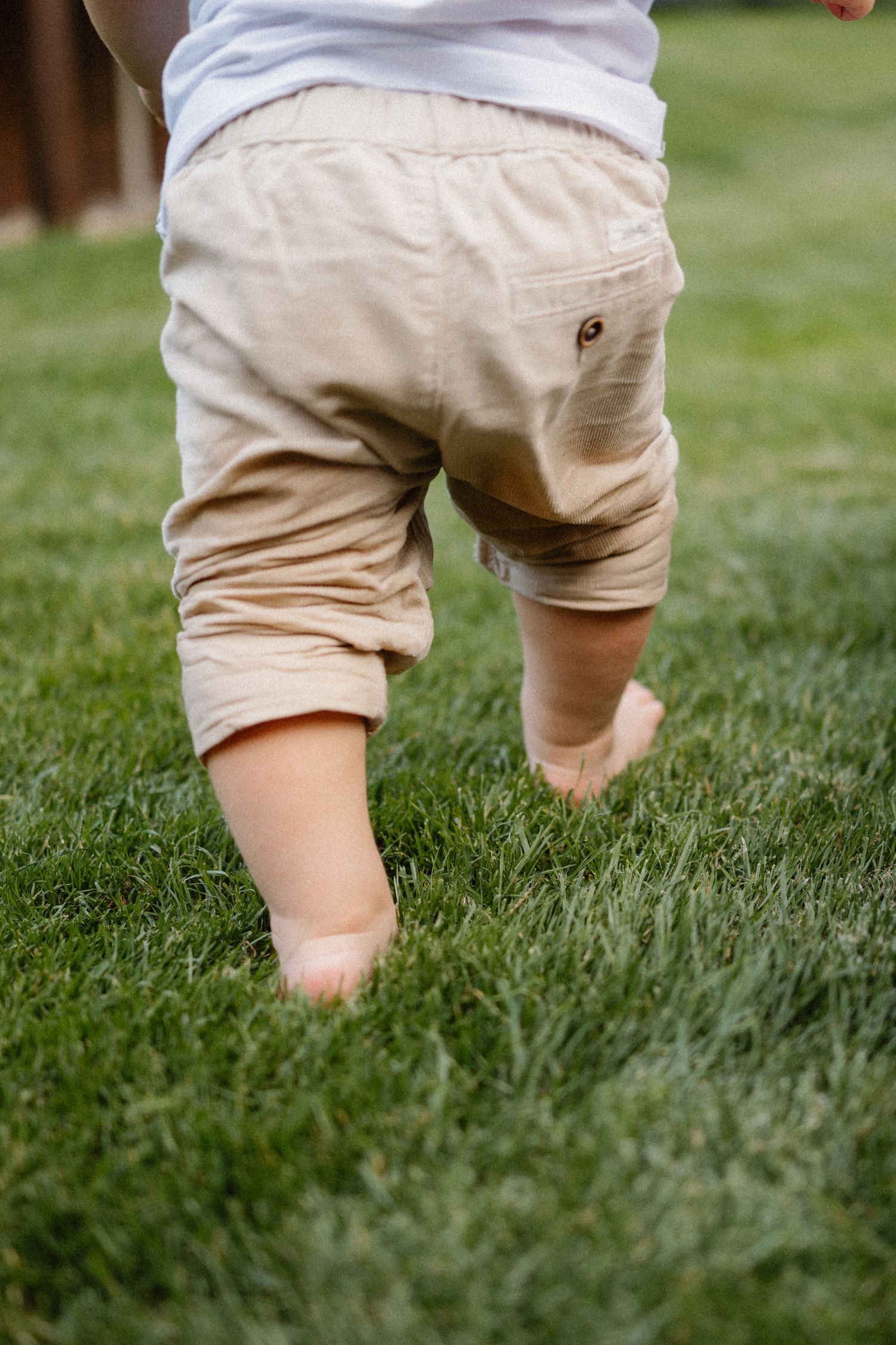 Close-up view of small legs in khaki shorts walking on green grass.