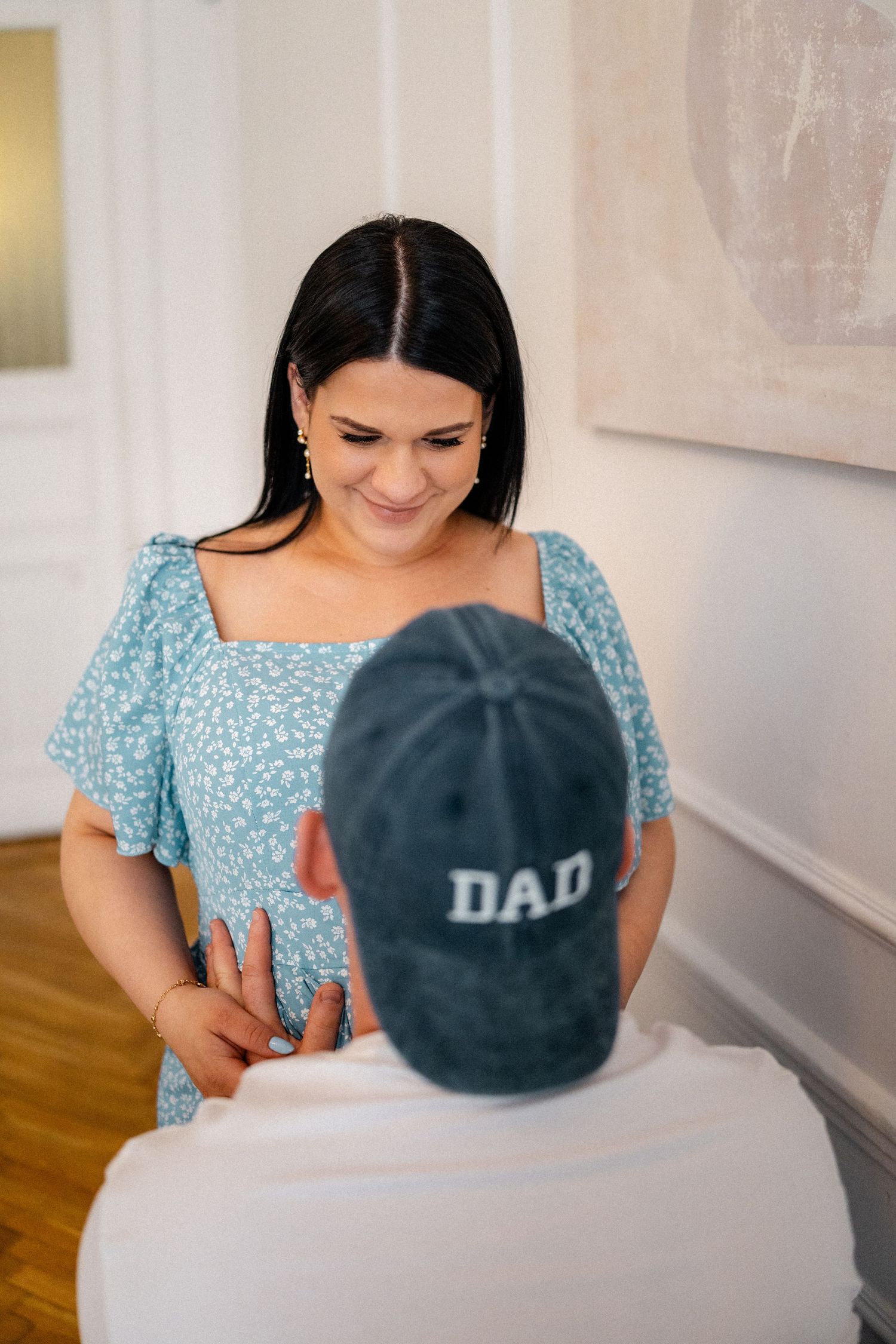 Pregnancy announcement scene with baseball caps and blue floral dress.