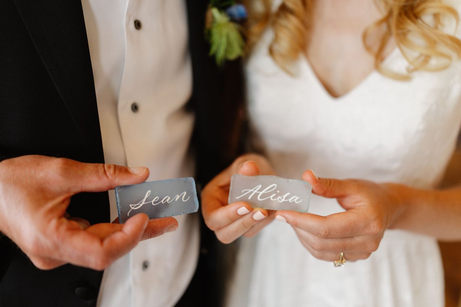 Bride and groom hold gray place cards with calligraphy names Sean and Alisa at wedding reception.