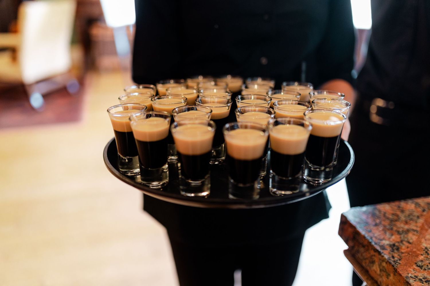 A server presents a tray of espresso martini shot glasses at an elegant wedding reception.