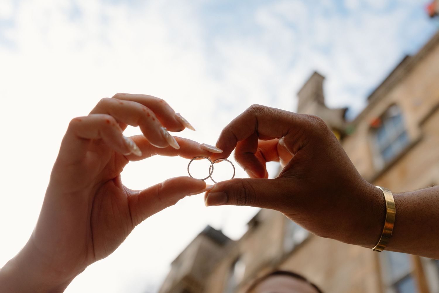 Two hands holding wedding rings together against a bright sky, symbolizing love and commitment.