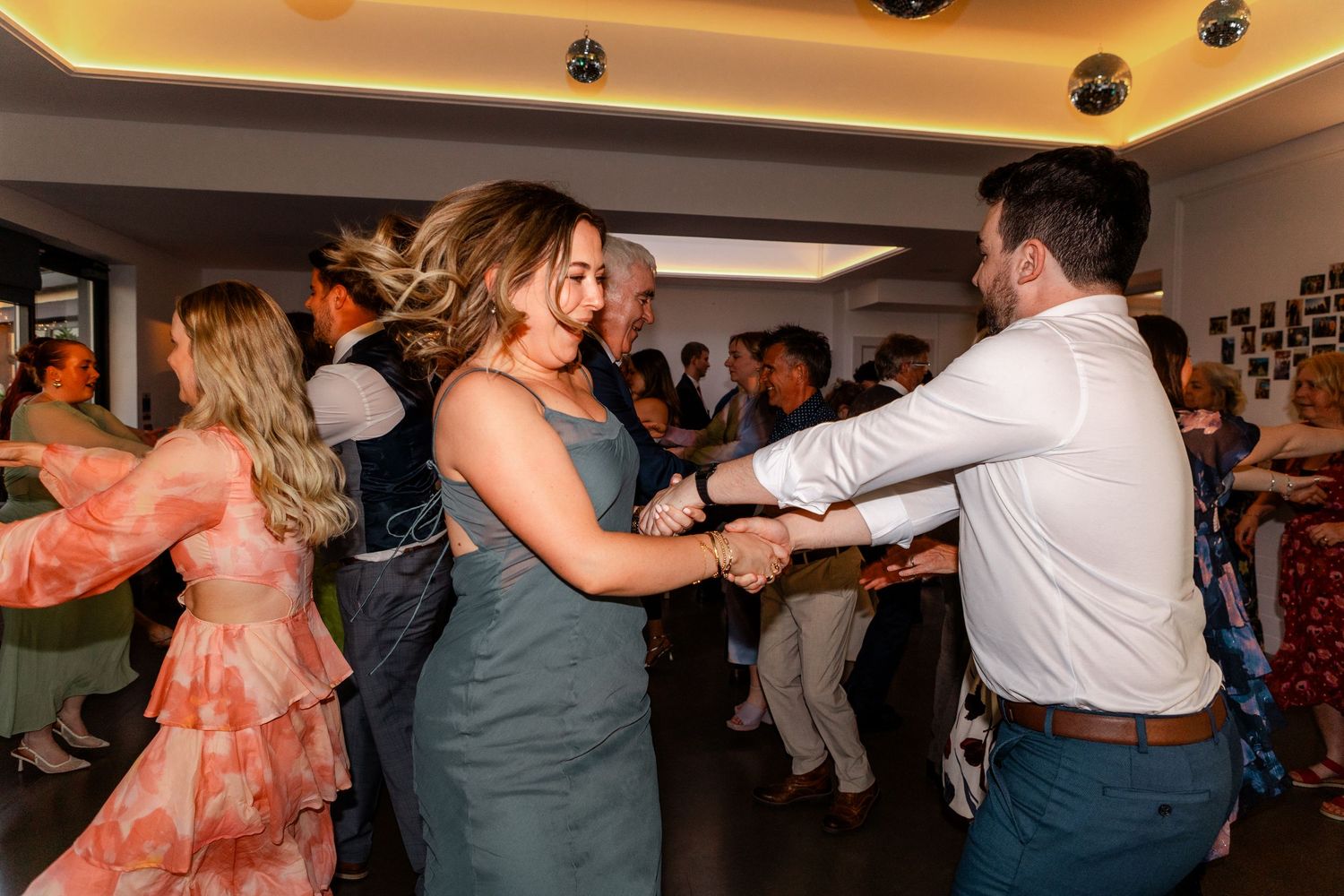 Guests enjoy energetic dancing at a lively wedding reception party in a warmly lit venue.