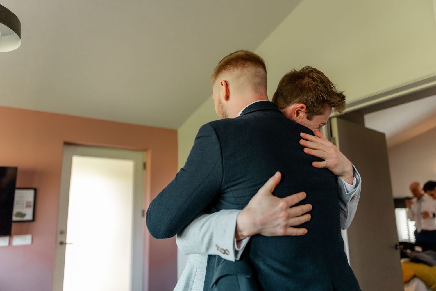 Two men in suits share a warm embrace during a wedding celebration.