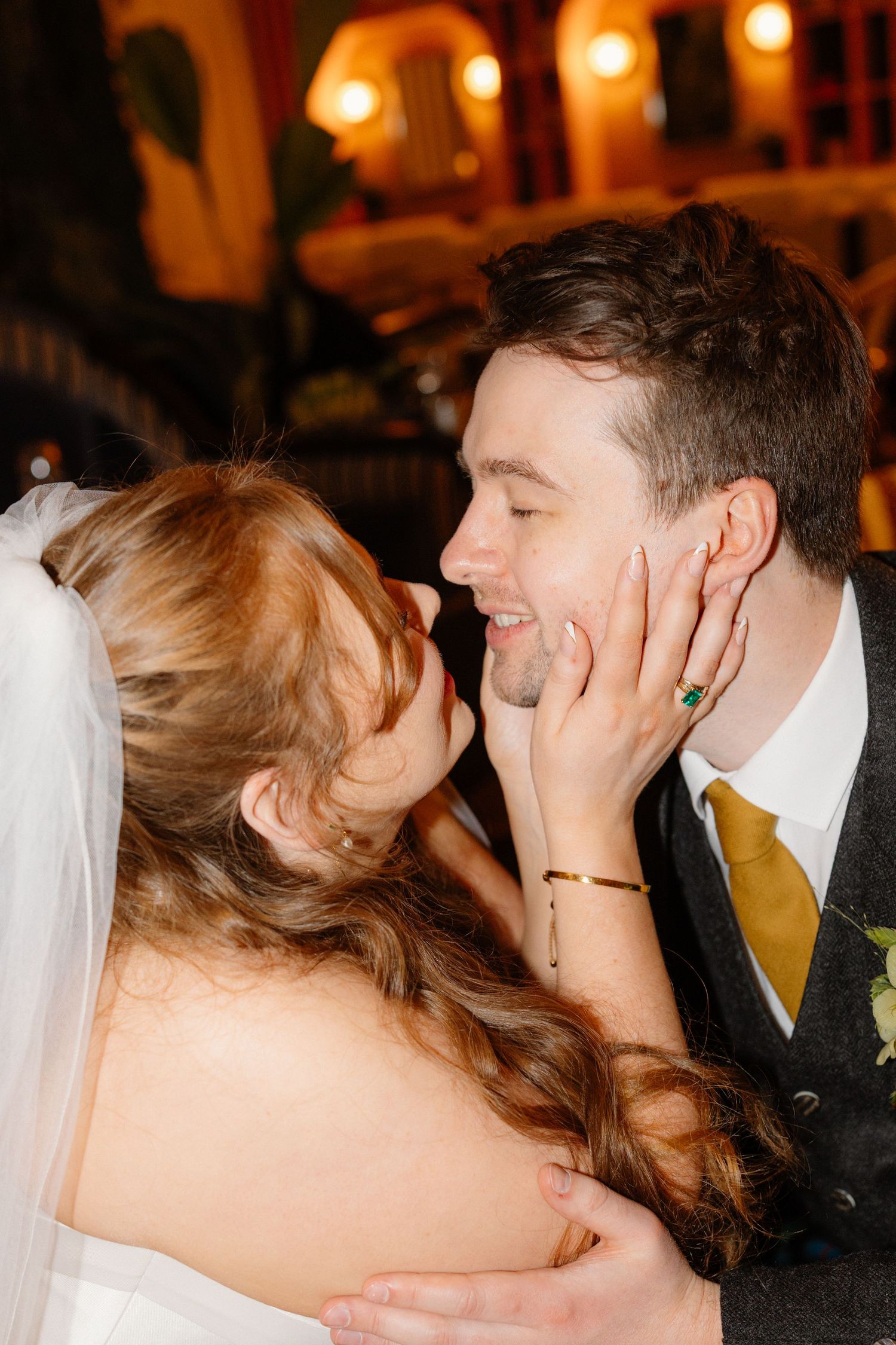 A joyful bride tenderly holds the groom's face as they share an intimate moment at their wedding reception.