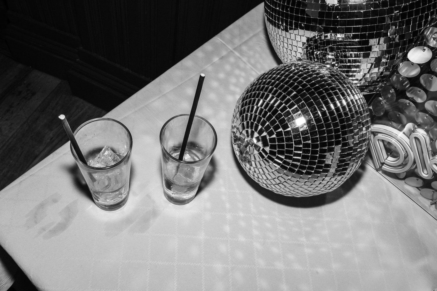 Black and white photo of two glasses with straws and a shiny disco ball on a white table.