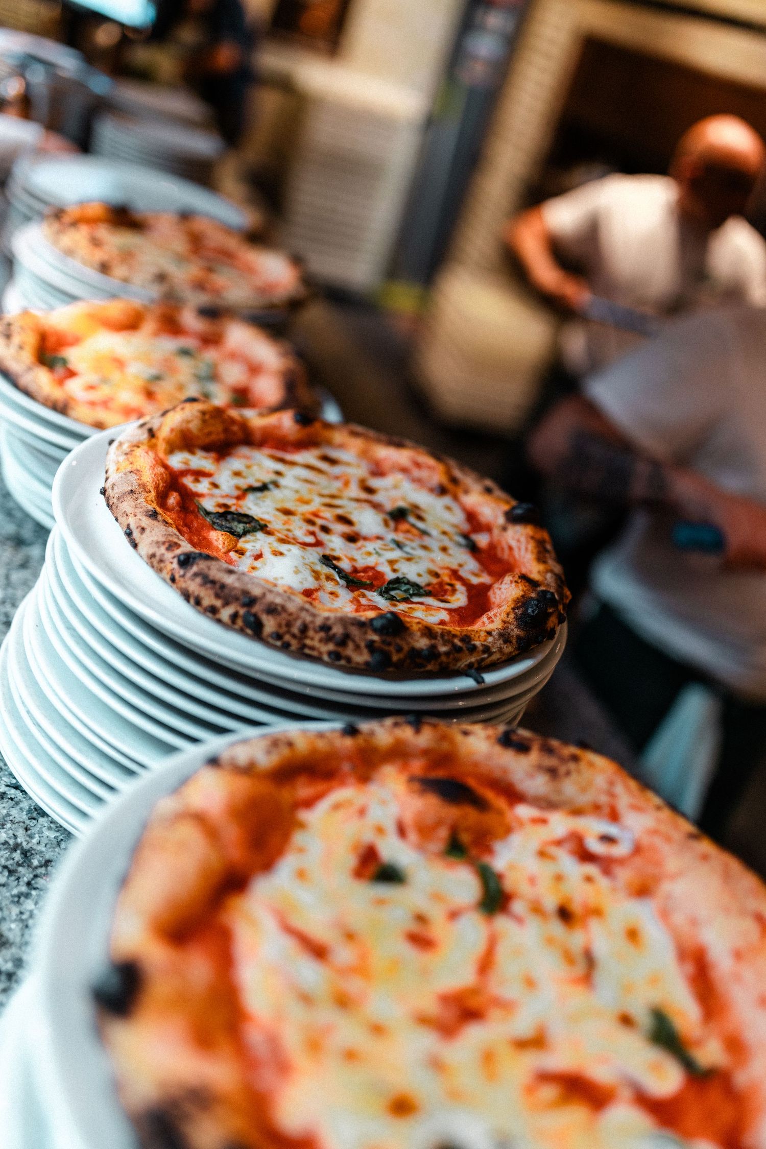 Fresh pizza pies with melted cheese and toppings lined up on white plates.