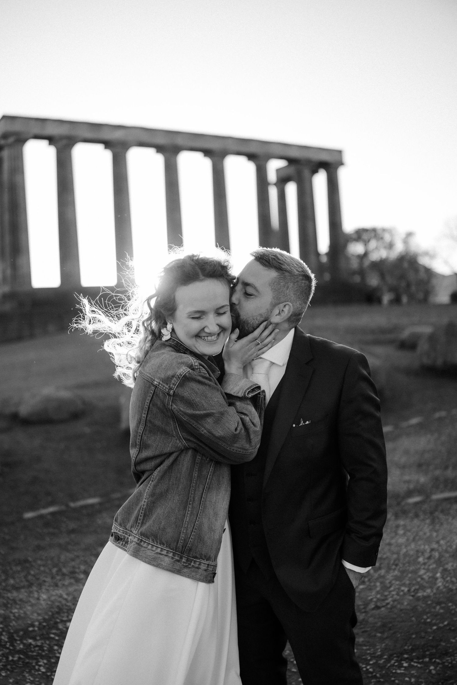 A romantic black and white photo of a couple embracing in front of ancient stone columns.