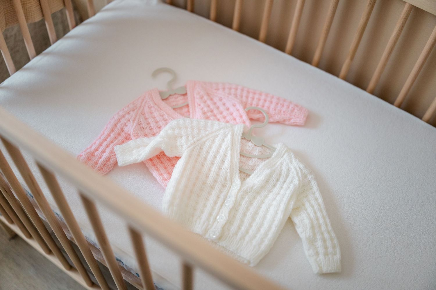 White knitted baby clothes laid out neatly on crib mattress.