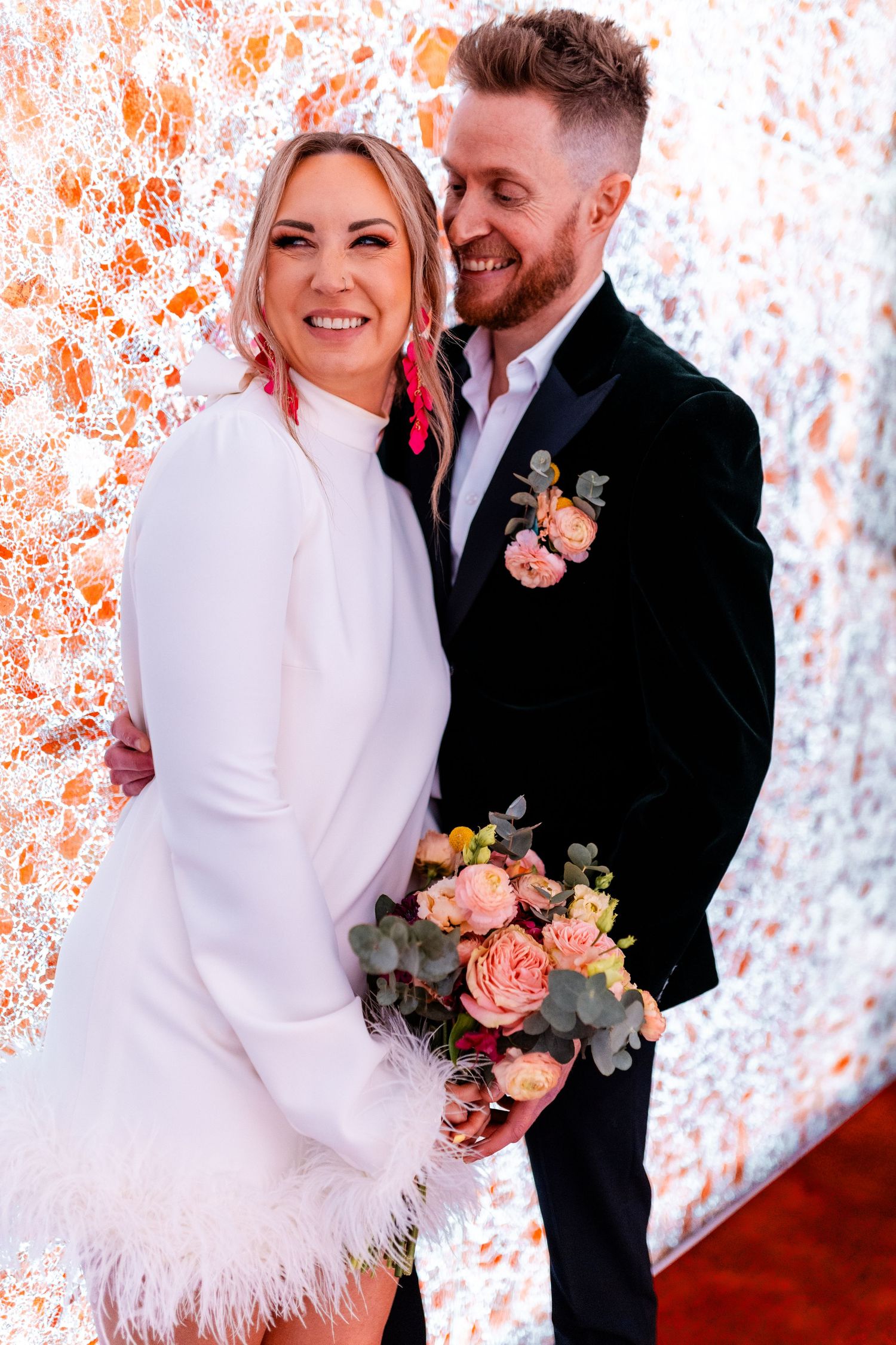 Wedding portraits against a coral-colored backdrop featuring a white dress with feather details.
