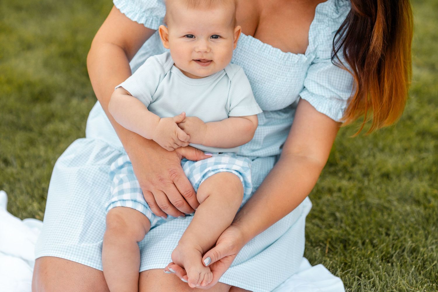 A family wearing coordinating light blue outfits sits together on green grass.