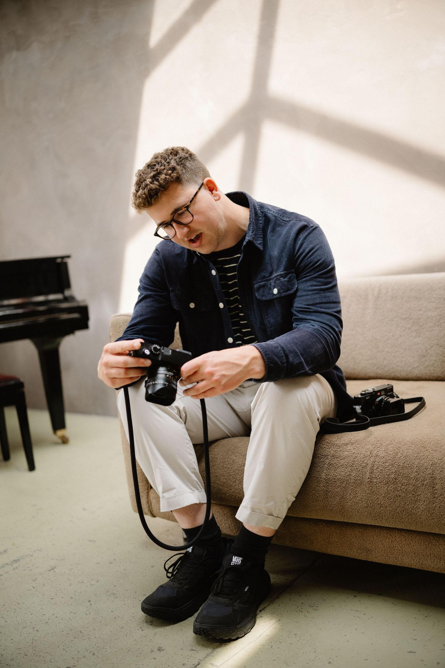 A photographer reviews images on their camera while sitting on a grey couch.