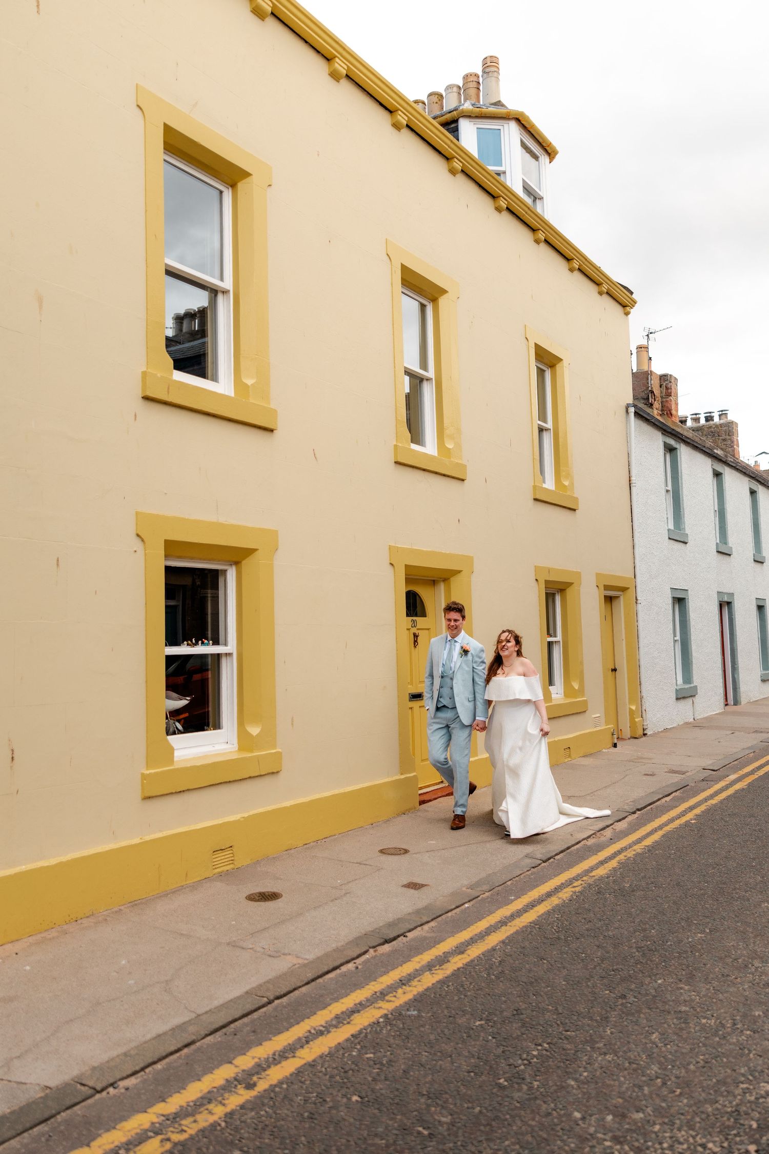 Wedding party walking along a yellow building with white trim.