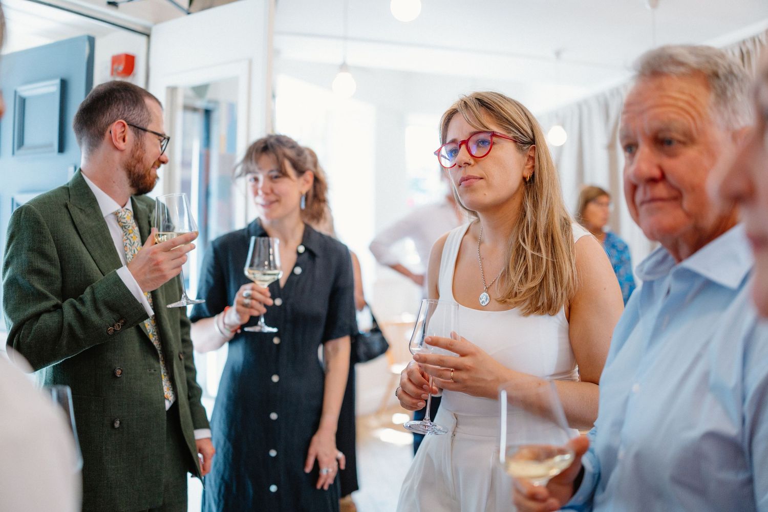 A group of people socializing and mingling at an indoor event with bright natural lighting.