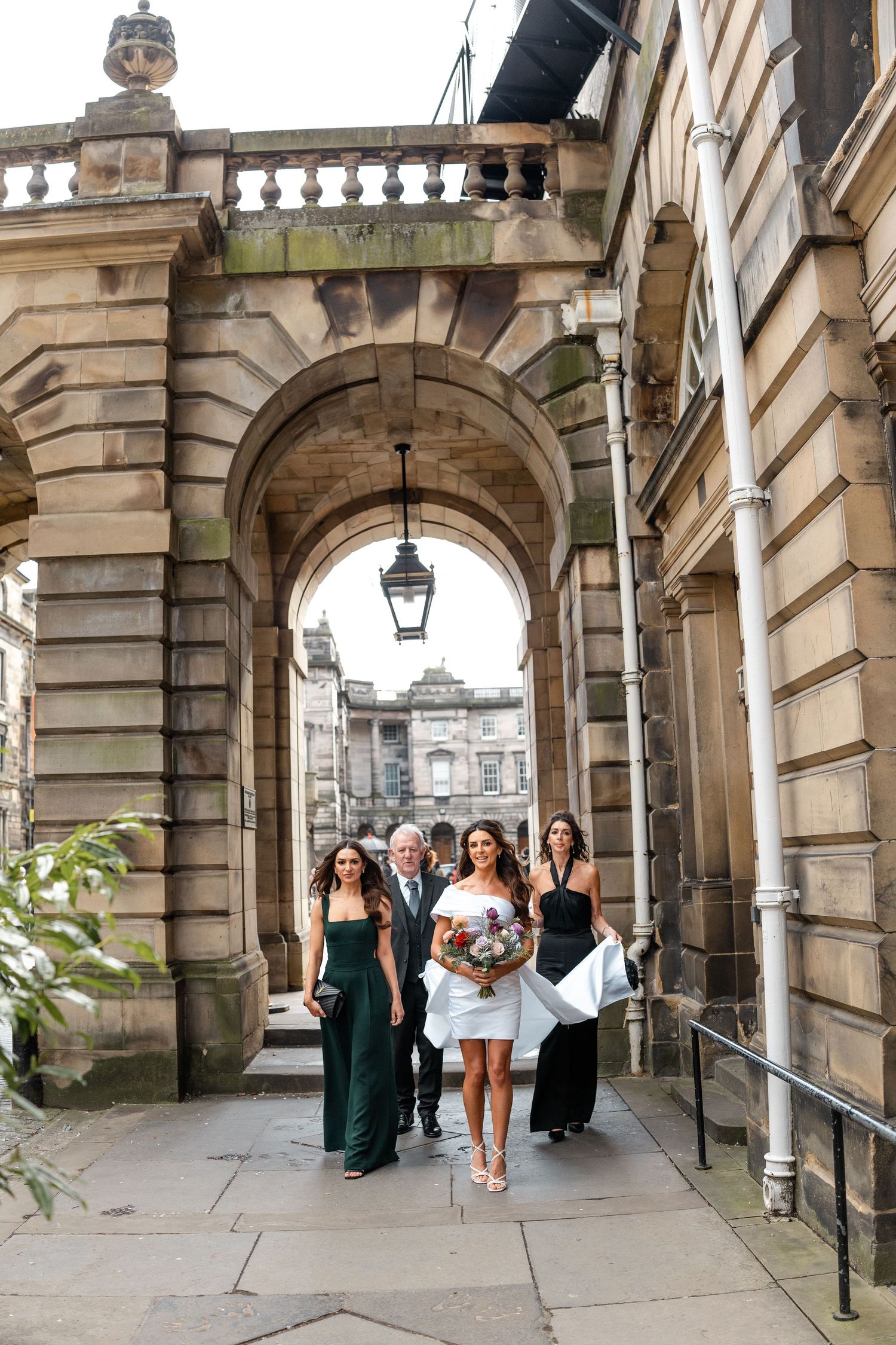 People walking through stone archways of a historic building during a formal event.