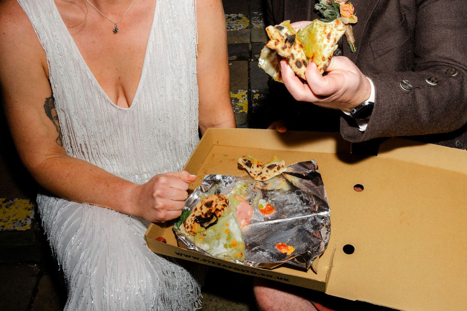 A couple sharing pizza from a cardboard box at a celebration.