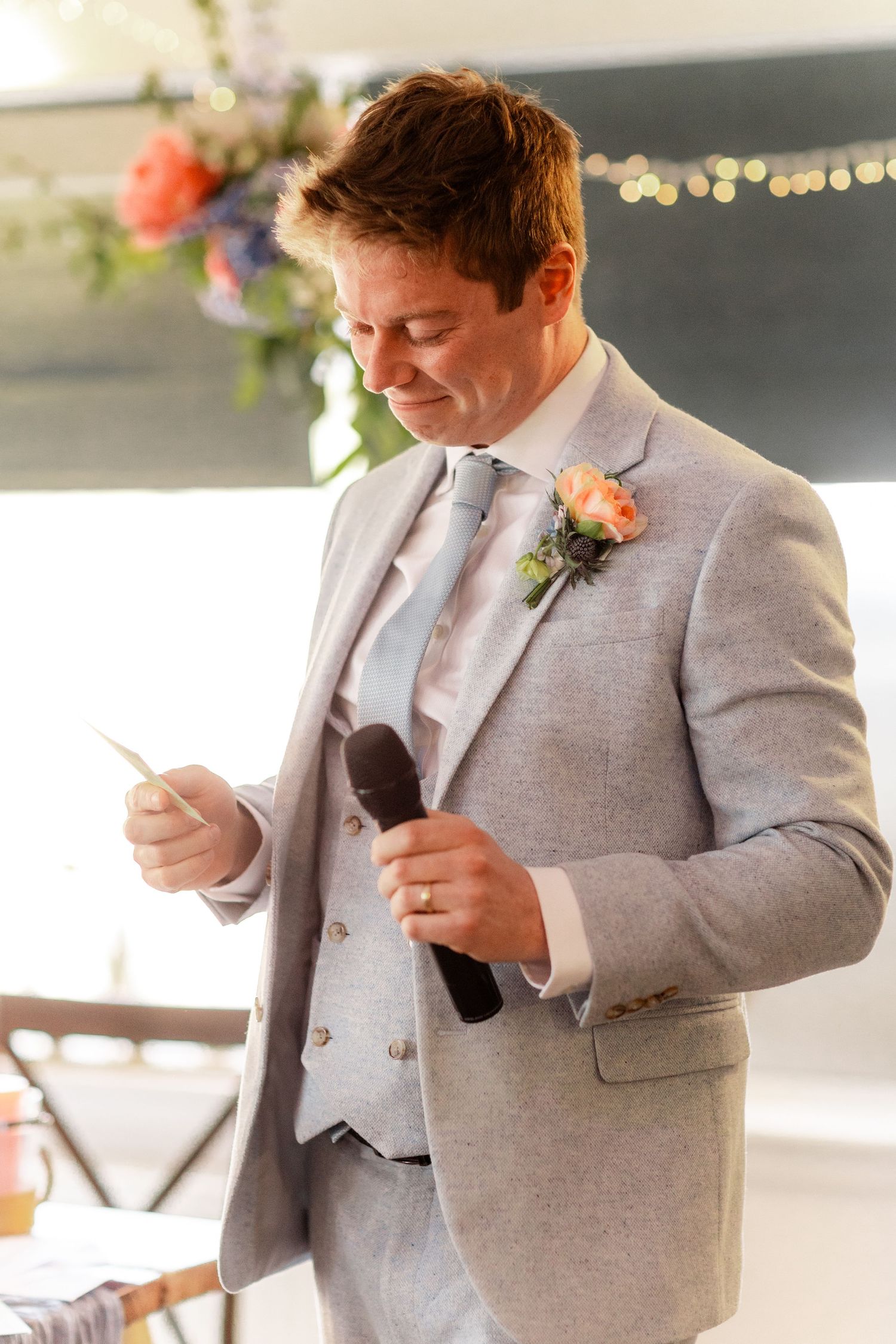 Someone in a light grey suit giving an emotional speech at a wedding reception.