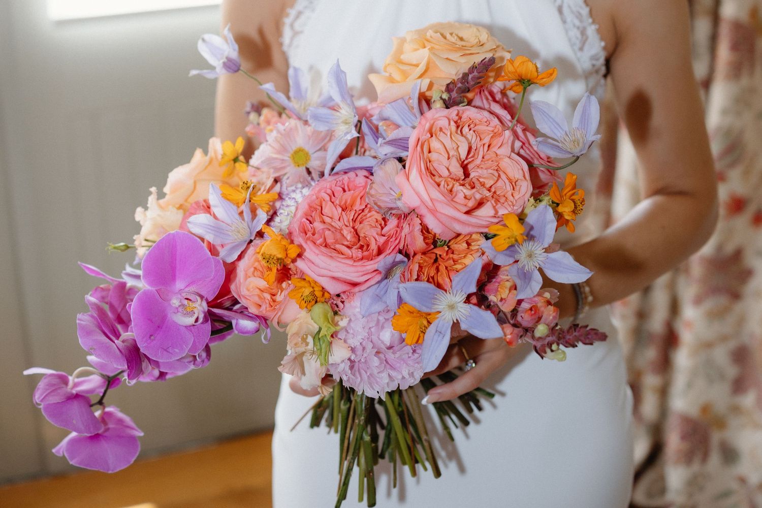 Vibrant bridal bouquet with pink, purple, and orange flowers against white dress.
