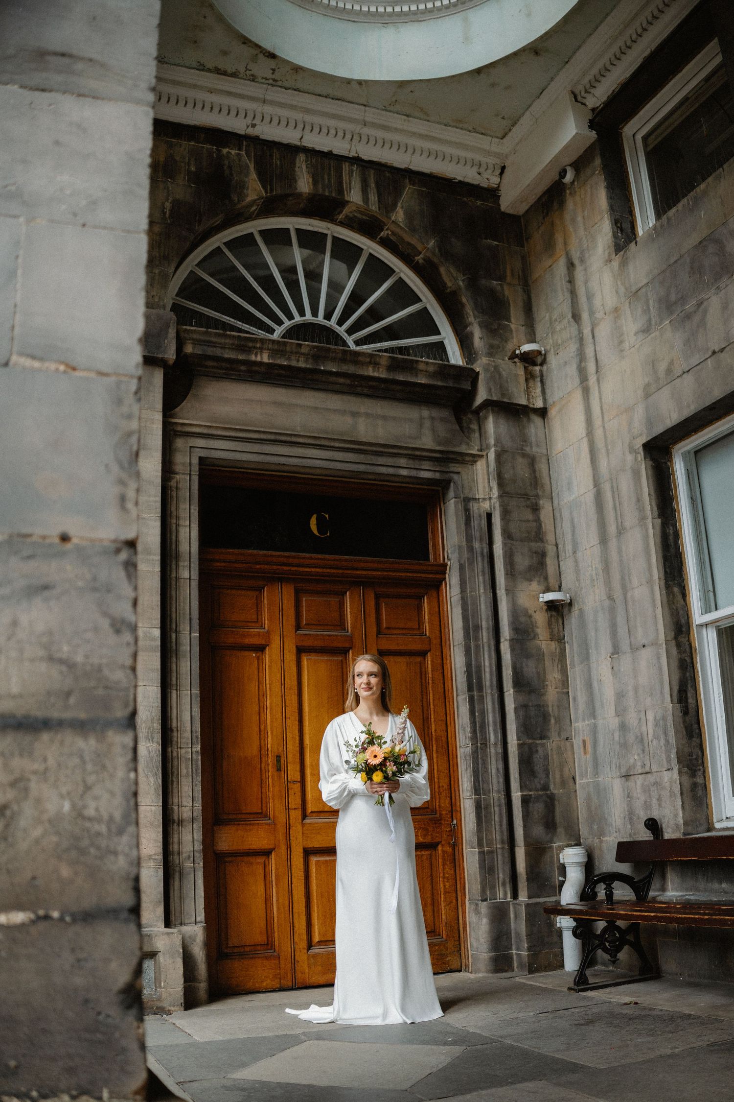 Elegant bride in white gown holds bouquet while standing before a wooden Georgian doorway.