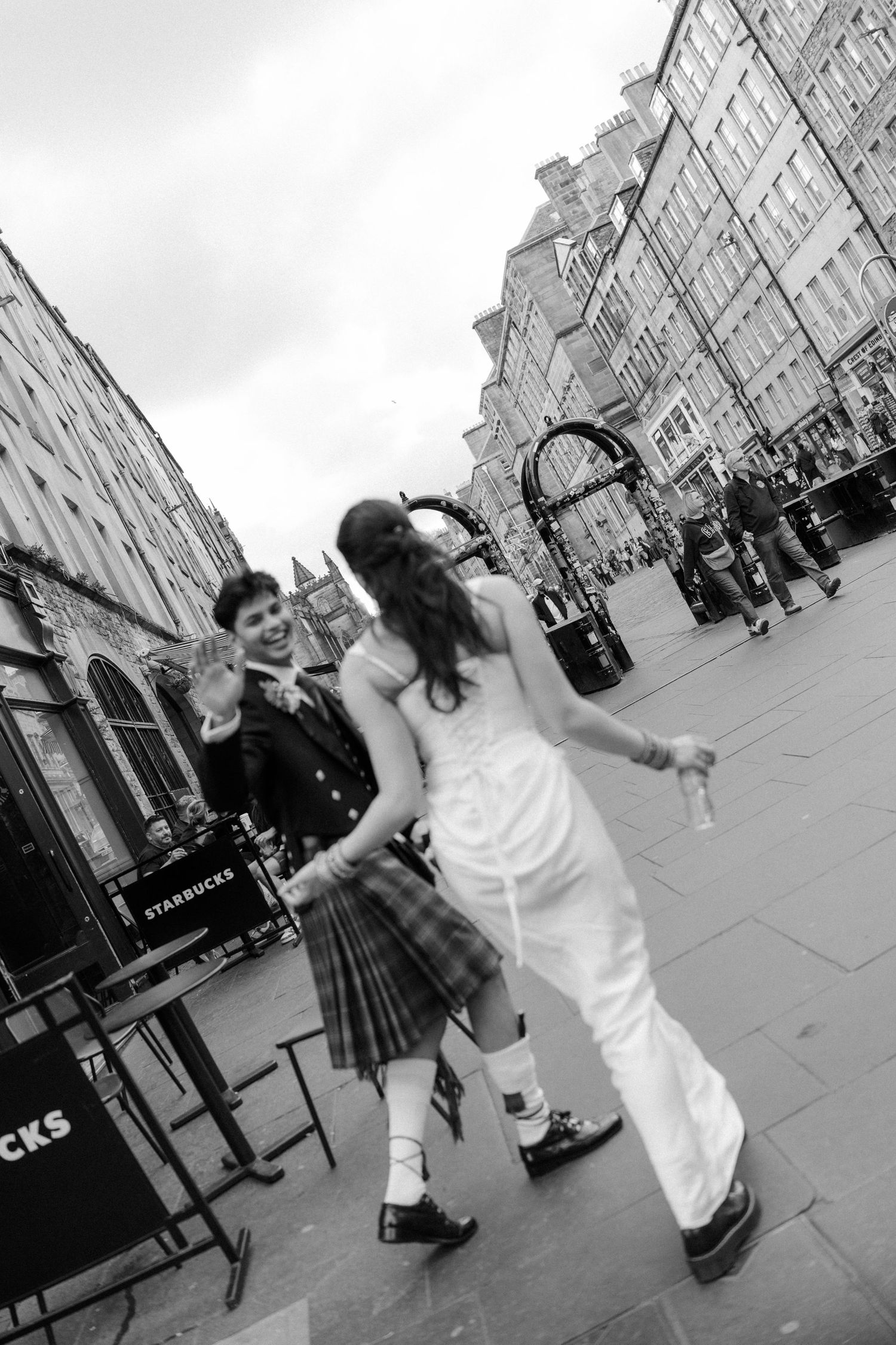 Black and white photo of newlywed couple dancing joyfully on Edinburgh's Royal Mile cobblestone street.