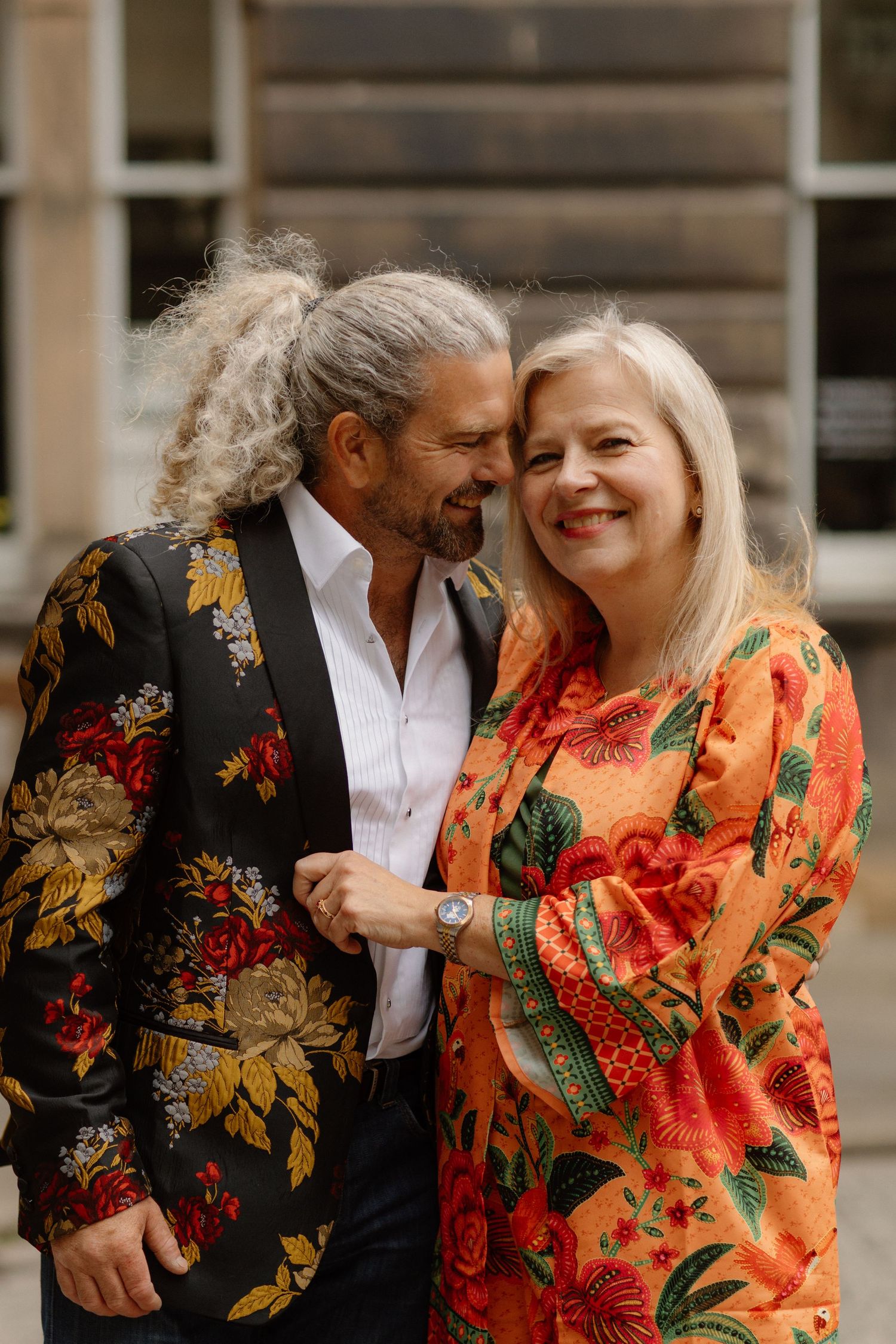 Mature couple in vibrant floral outfits share a romantic moment on an Edinburgh street.