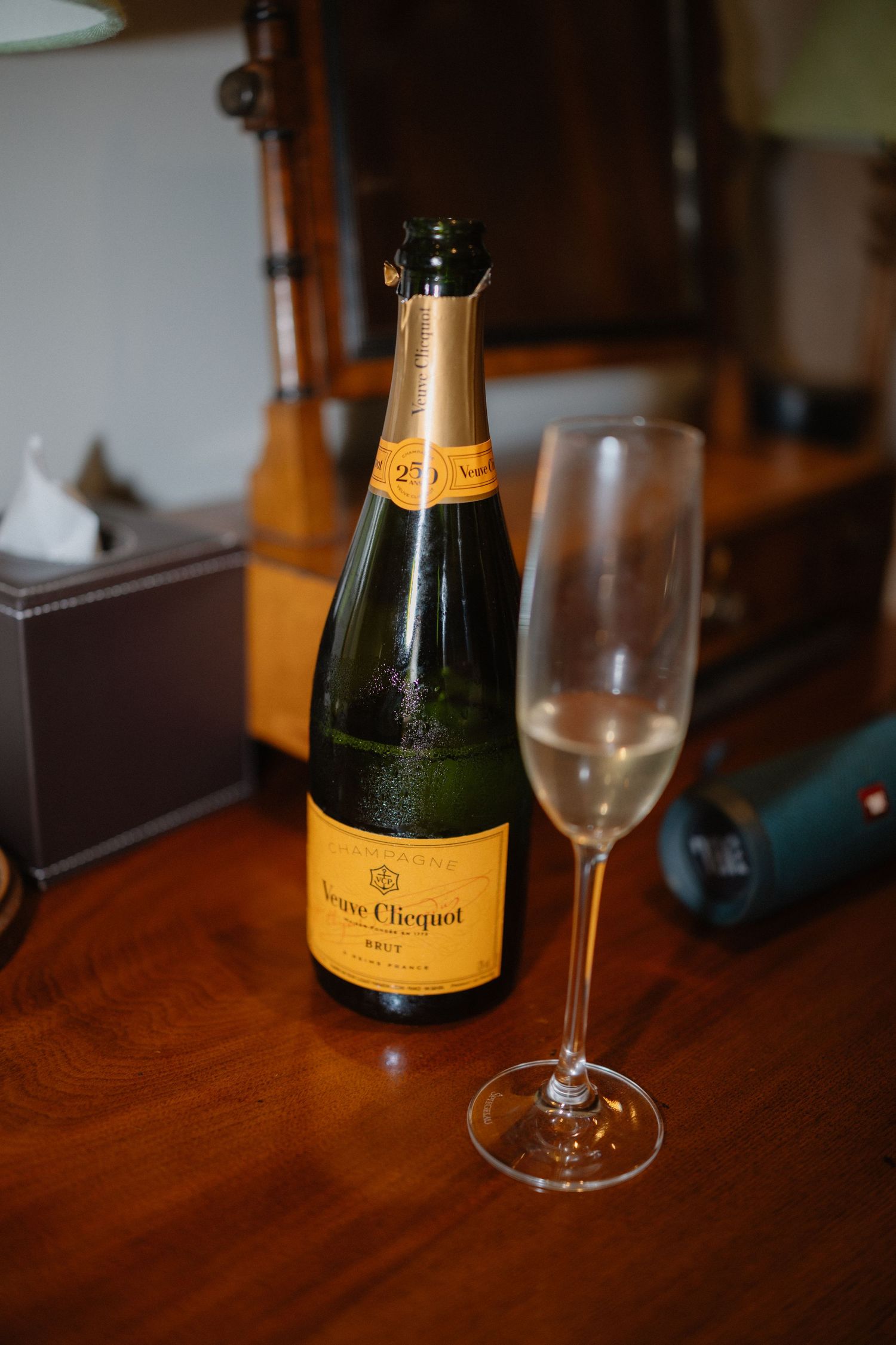 Bottle of Veuve Clicquot Brut champagne beside a filled flute glass on a wooden table.