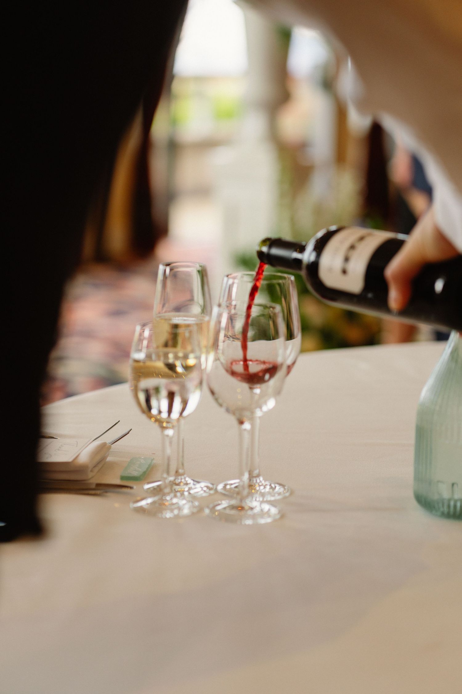 Waiter pouring red wine into glass beside white wine at elegant wedding reception.