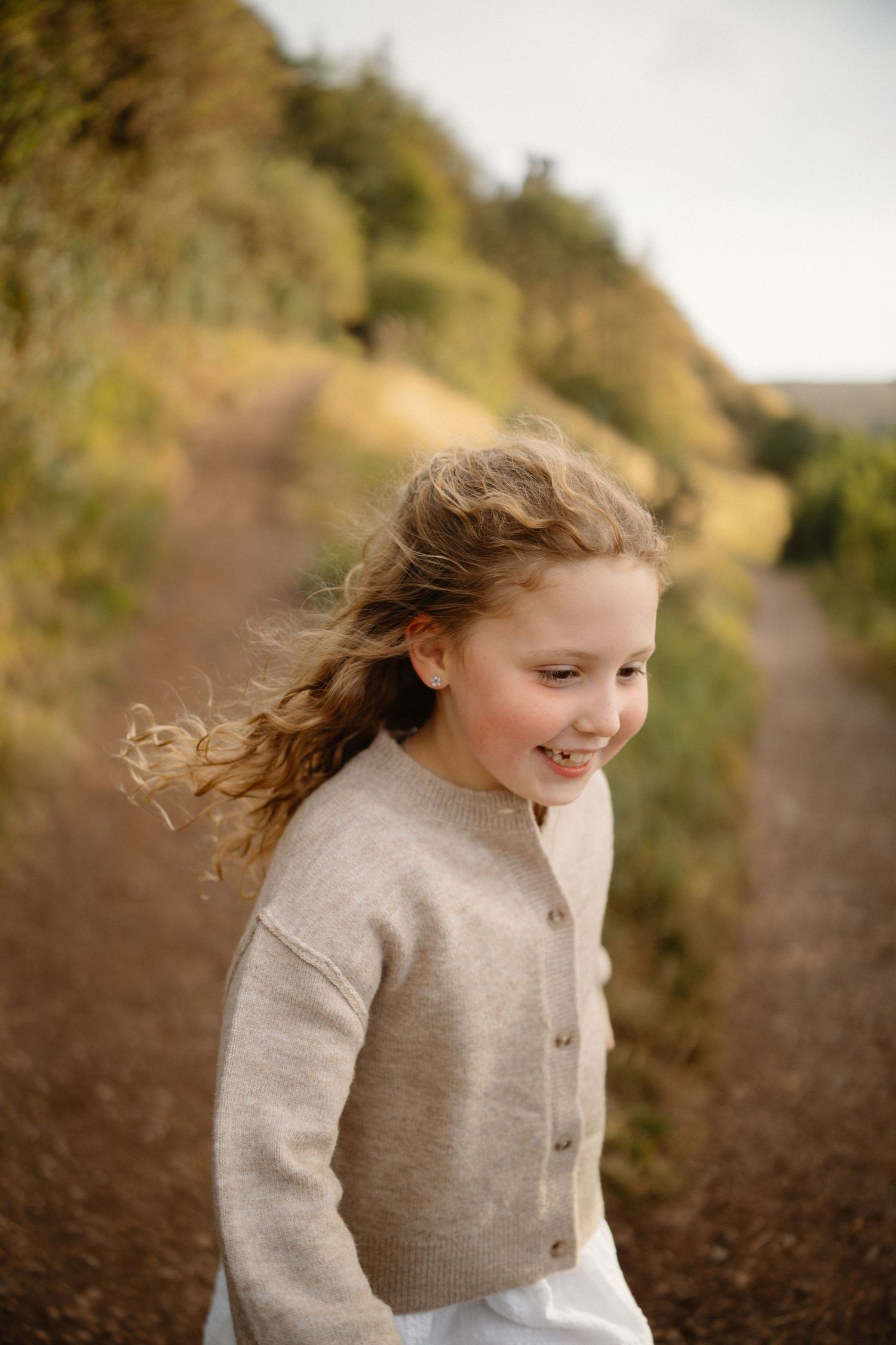 Child with flowing hair runs joyfully on outdoor trail.