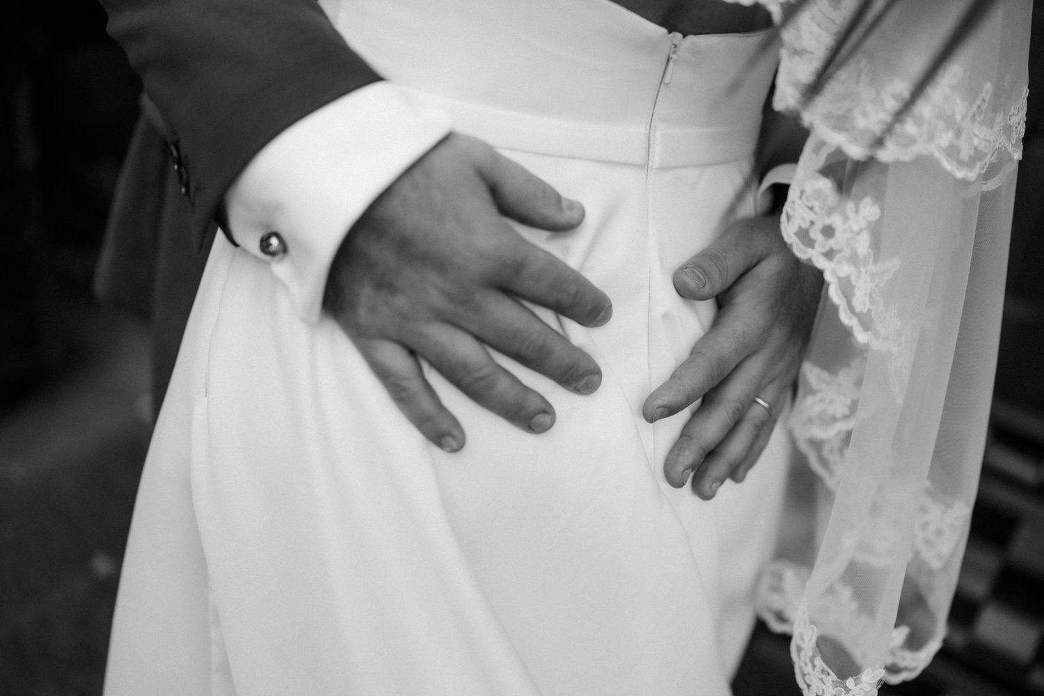 Close-up black and white photo of hands touching a white wedding dress.